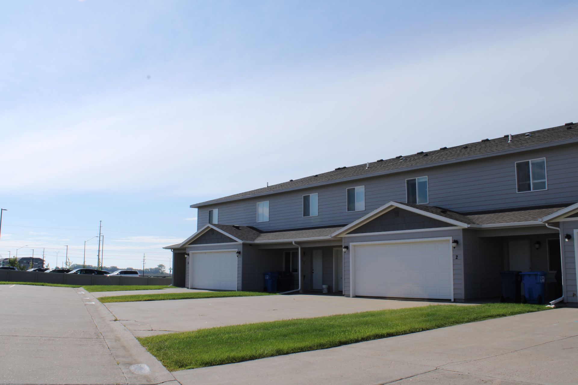 Row of modern townhouses with attached garages along a quiet suburban street under a blue sky