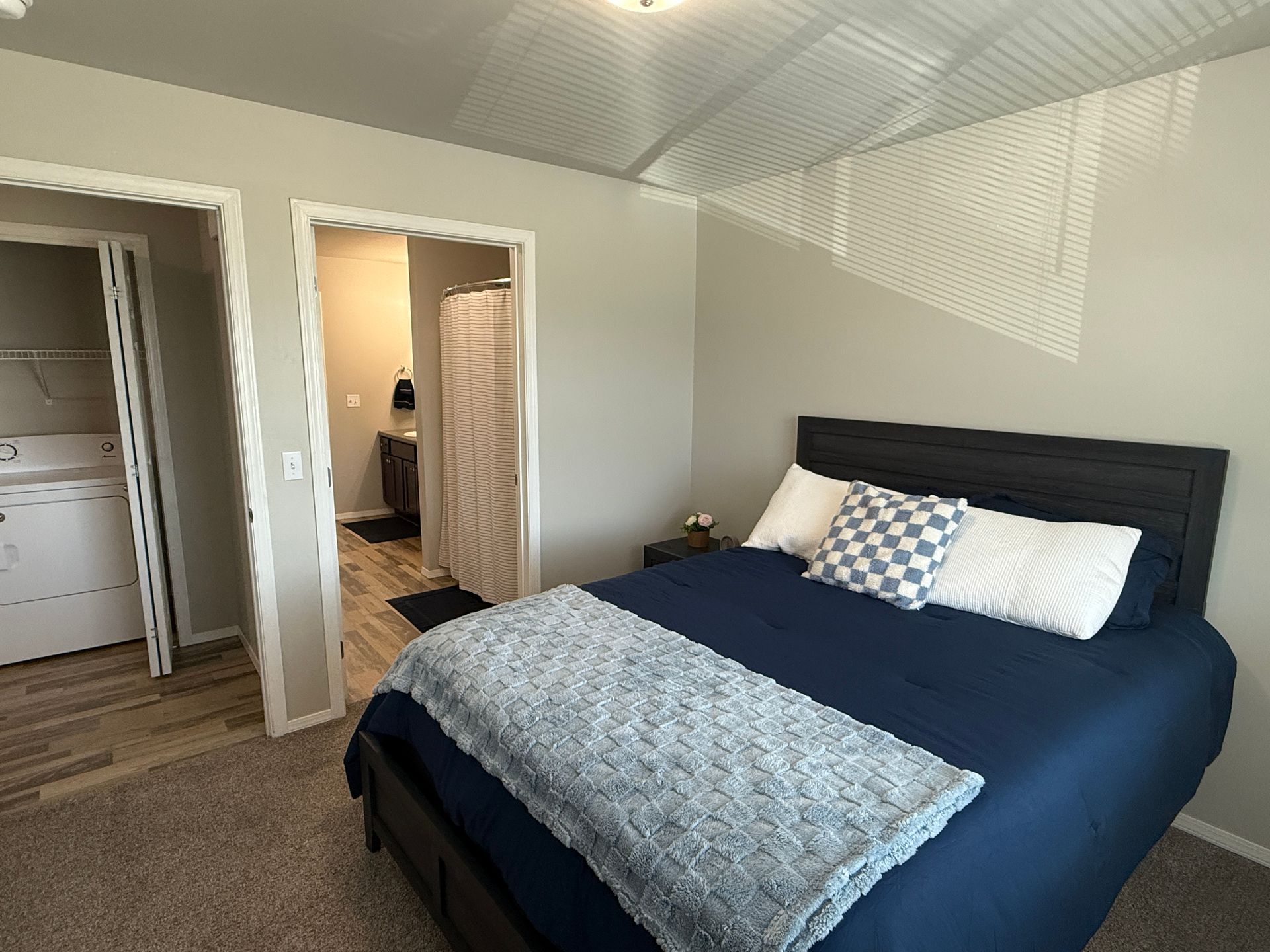 Bright bedroom with a navy bed, blue-gray walls, white trim, and an open doorway to a bathroom.