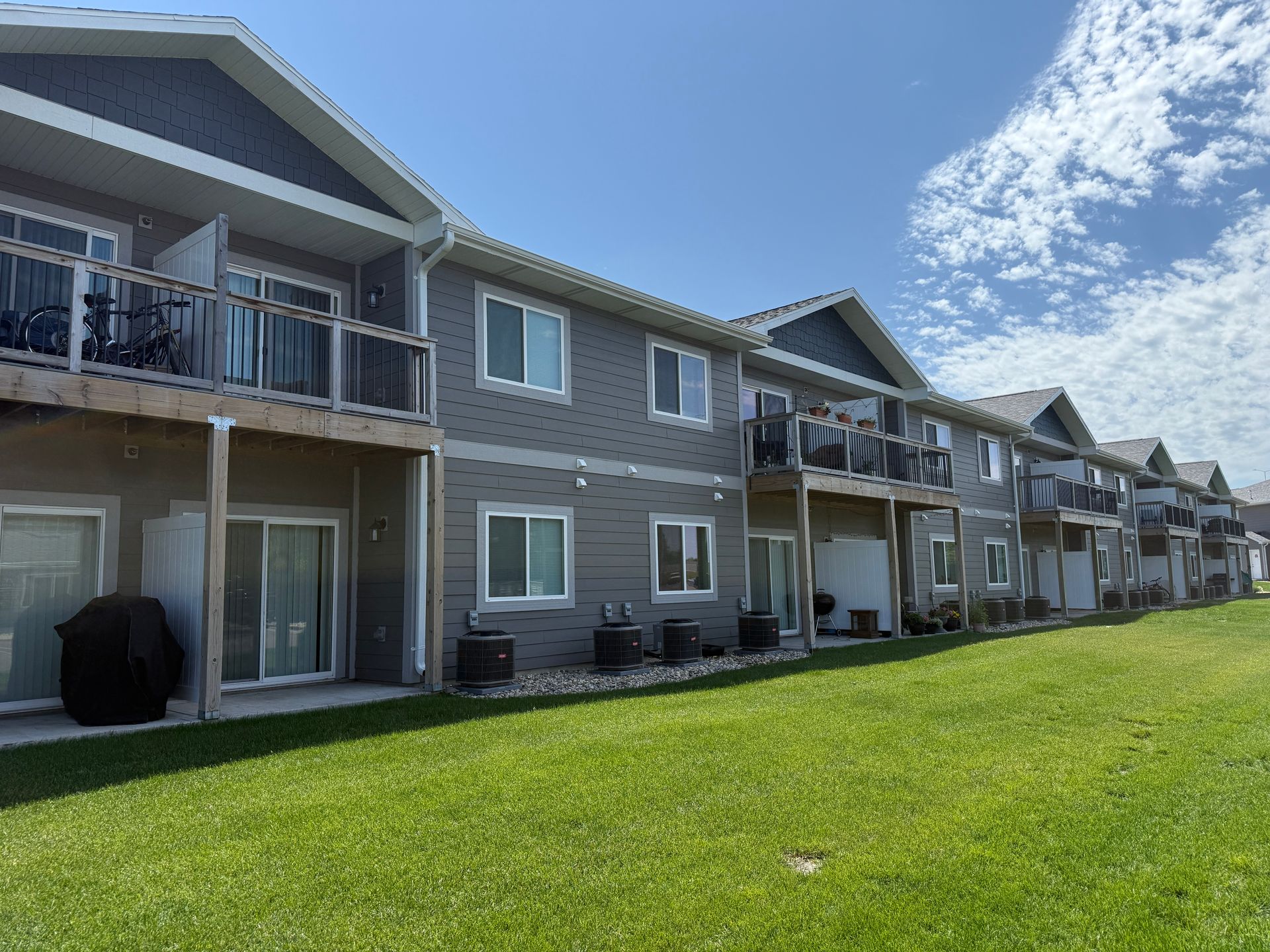 Row of gray apartment balconies beside a green lawn under a blue sky