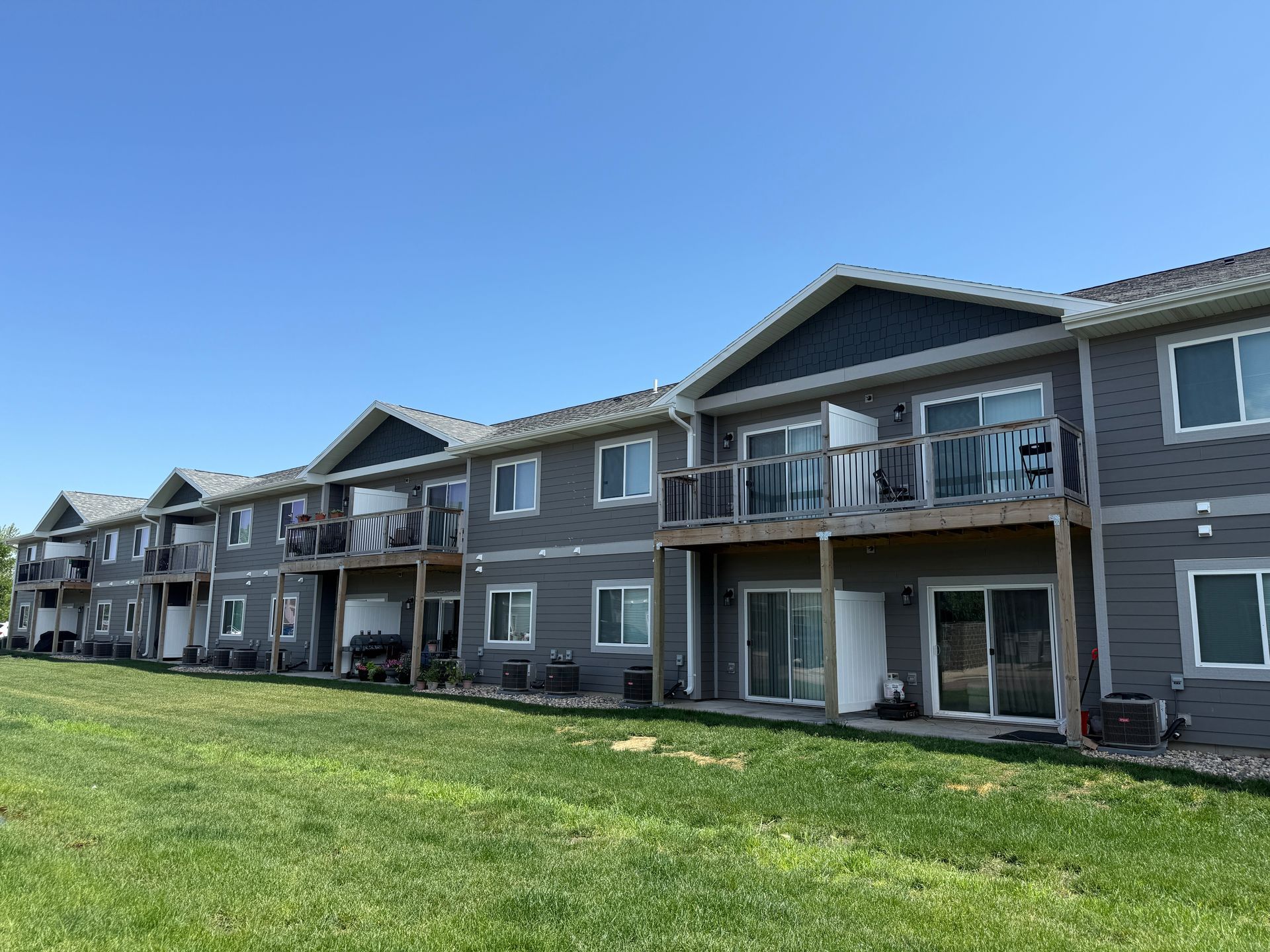 Row of gray apartment balconies beside a green lawn under a blue sky