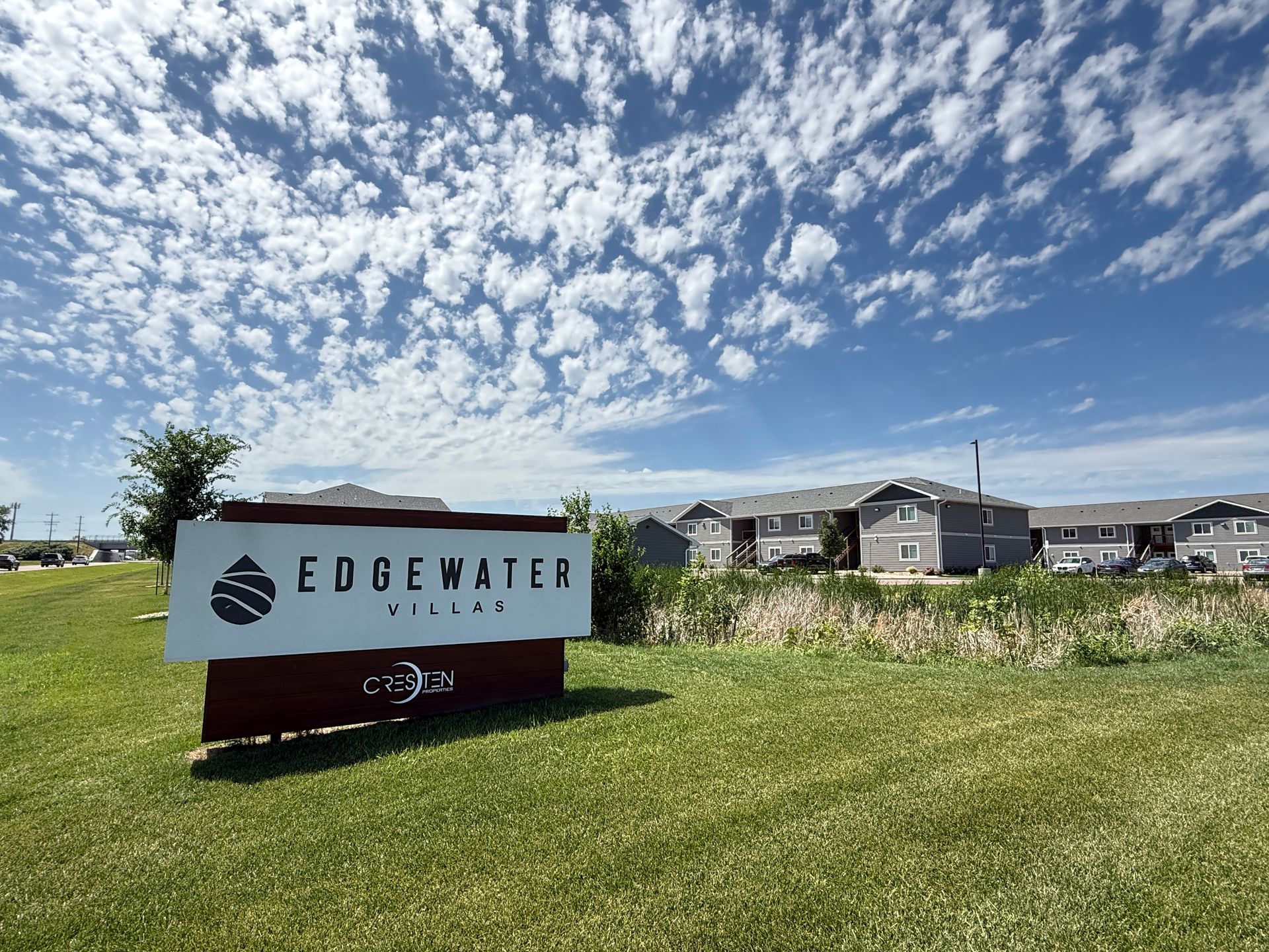 Edgewater Village sign on a grassy field under a bright blue, cloud-filled sky with homes in the background