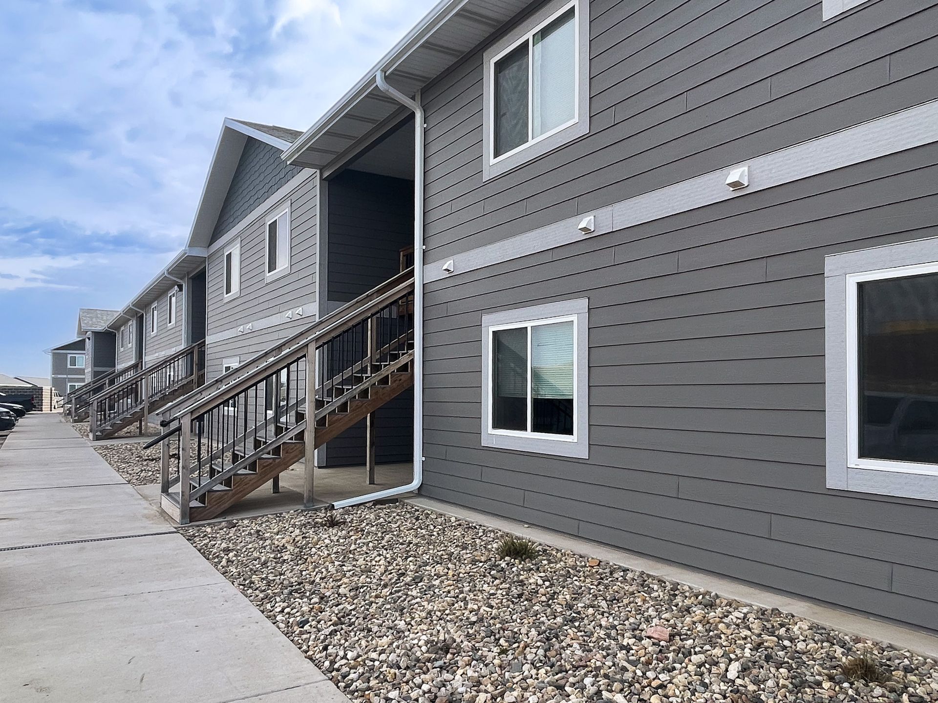Gray apartment building exterior with staircases and balconies along a gravel walkway