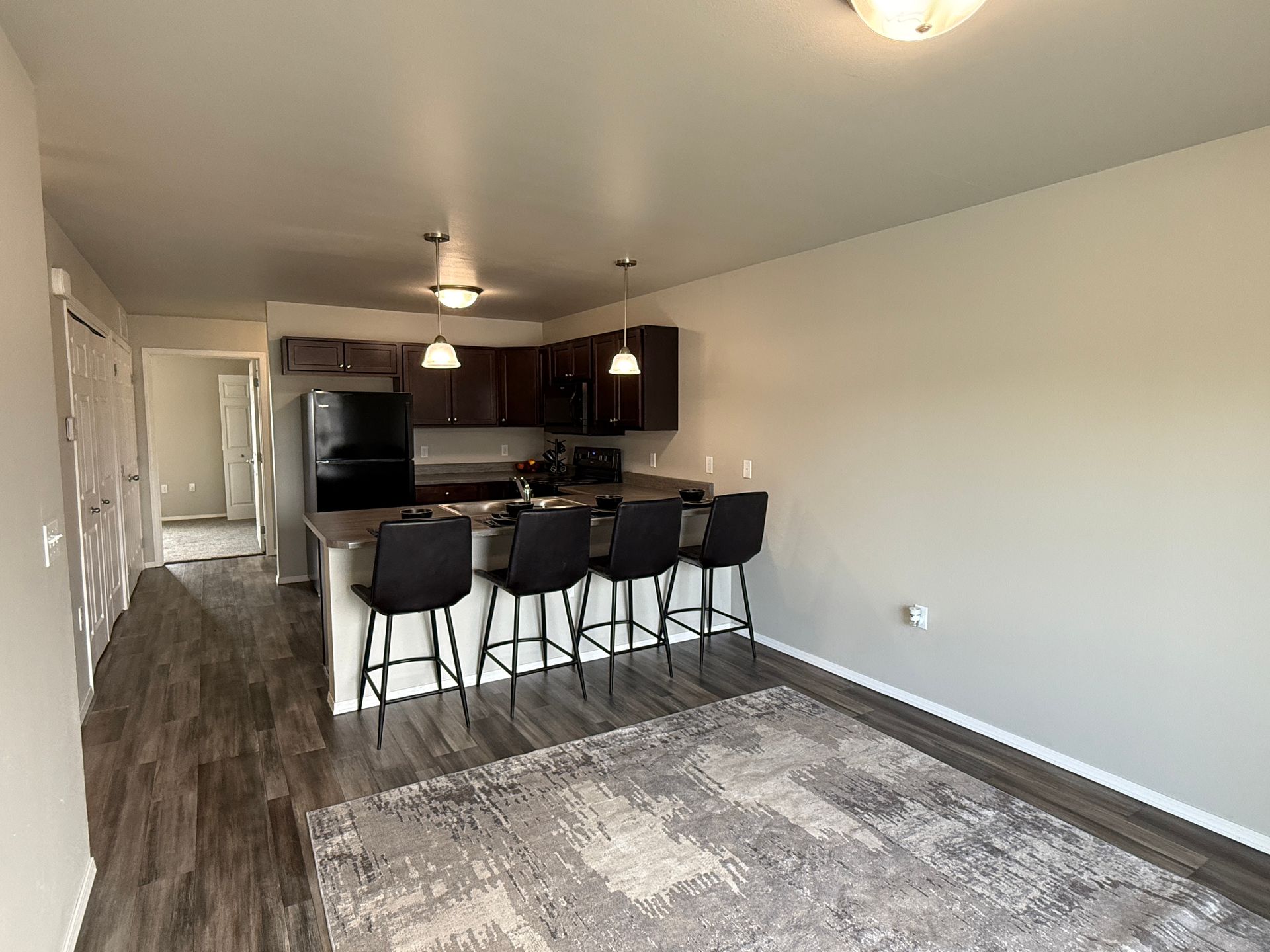 Modern open-plan living room with kitchen island, dark bar stools, and gray patterned rug