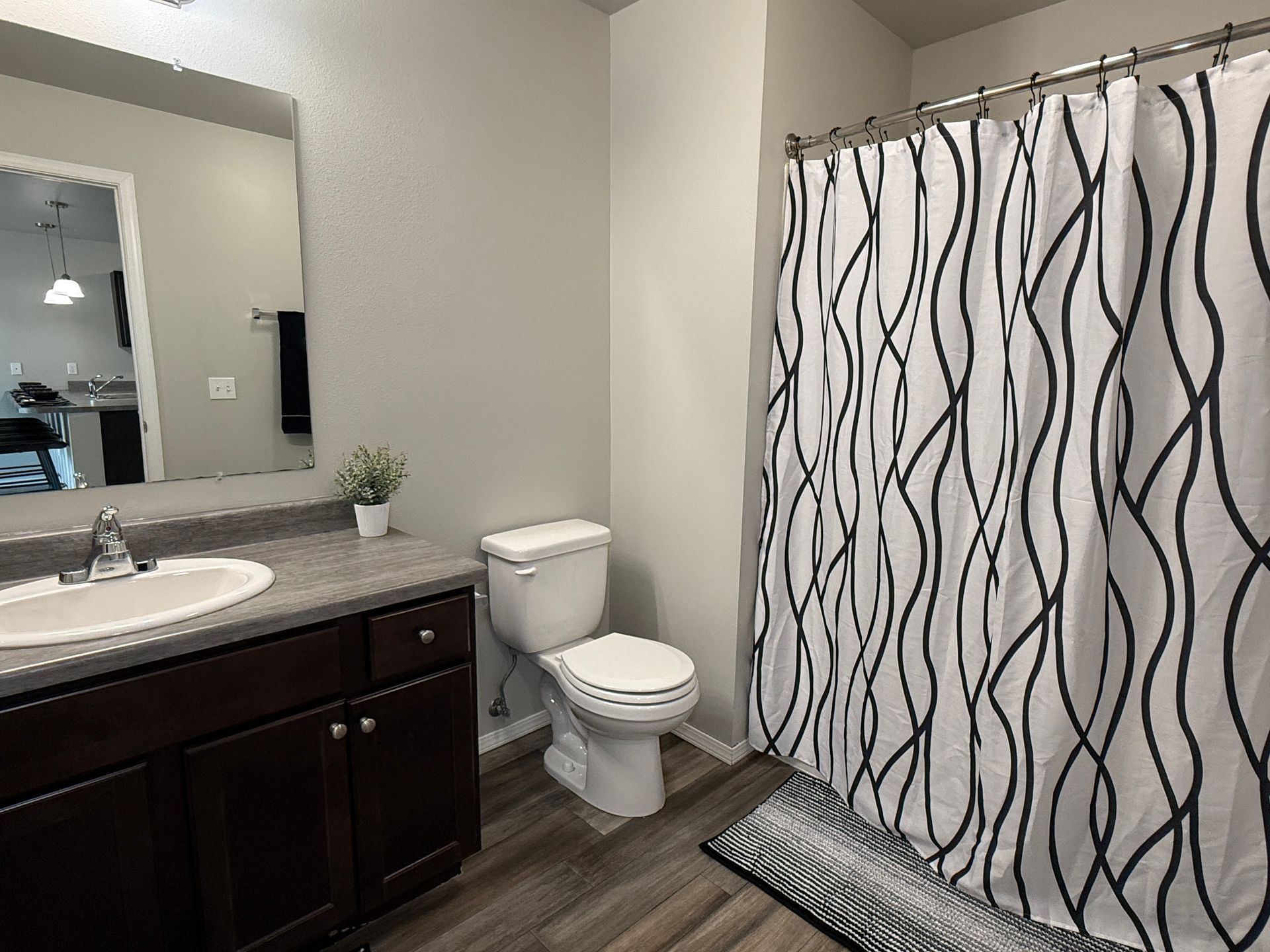 Small bathroom with dark vanity, sink, toilet, mirror, and black-and-white wavy shower curtain.