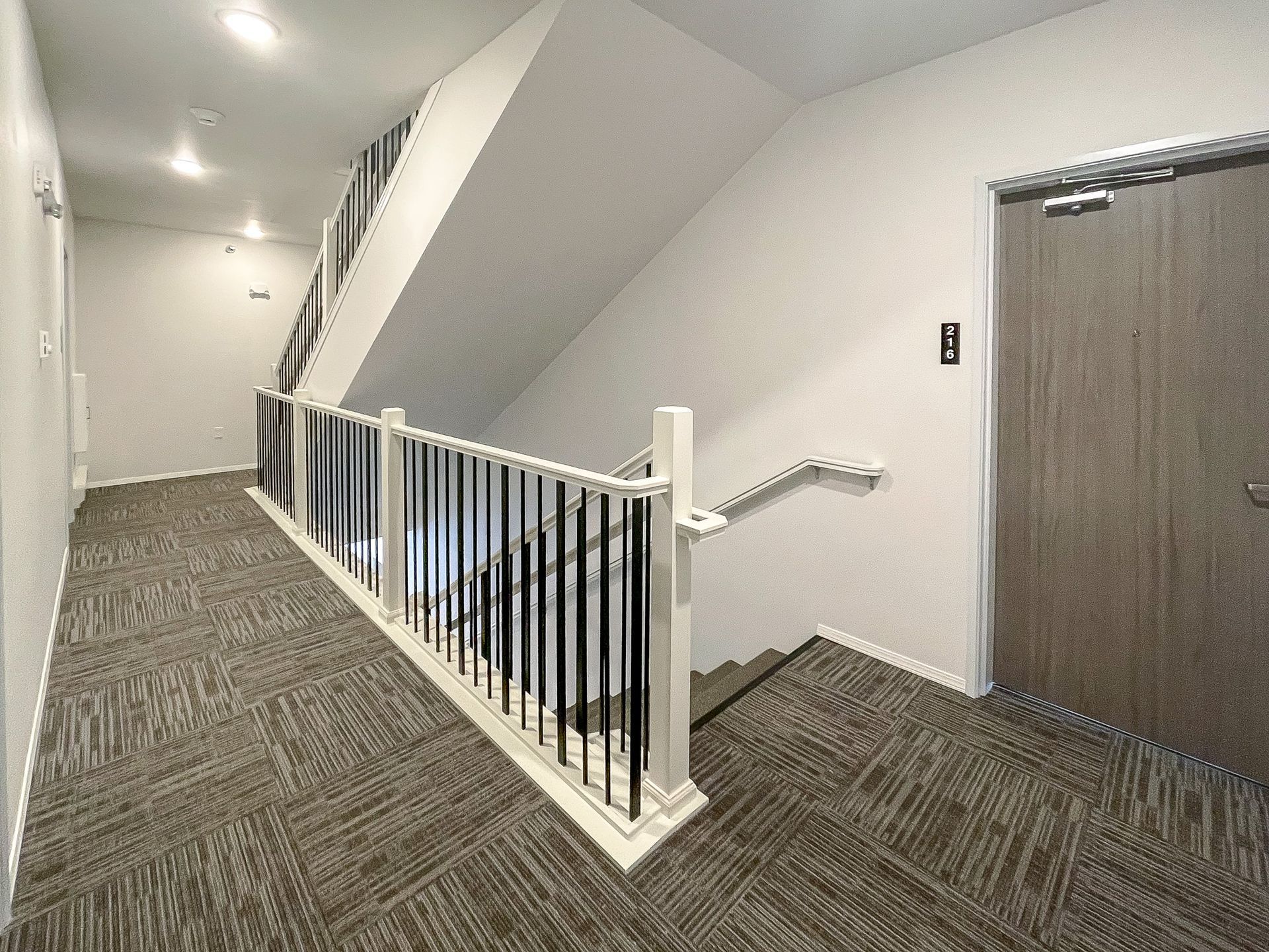 Hallway with carpeted floor, white railing, and gray doors in an apartment building
