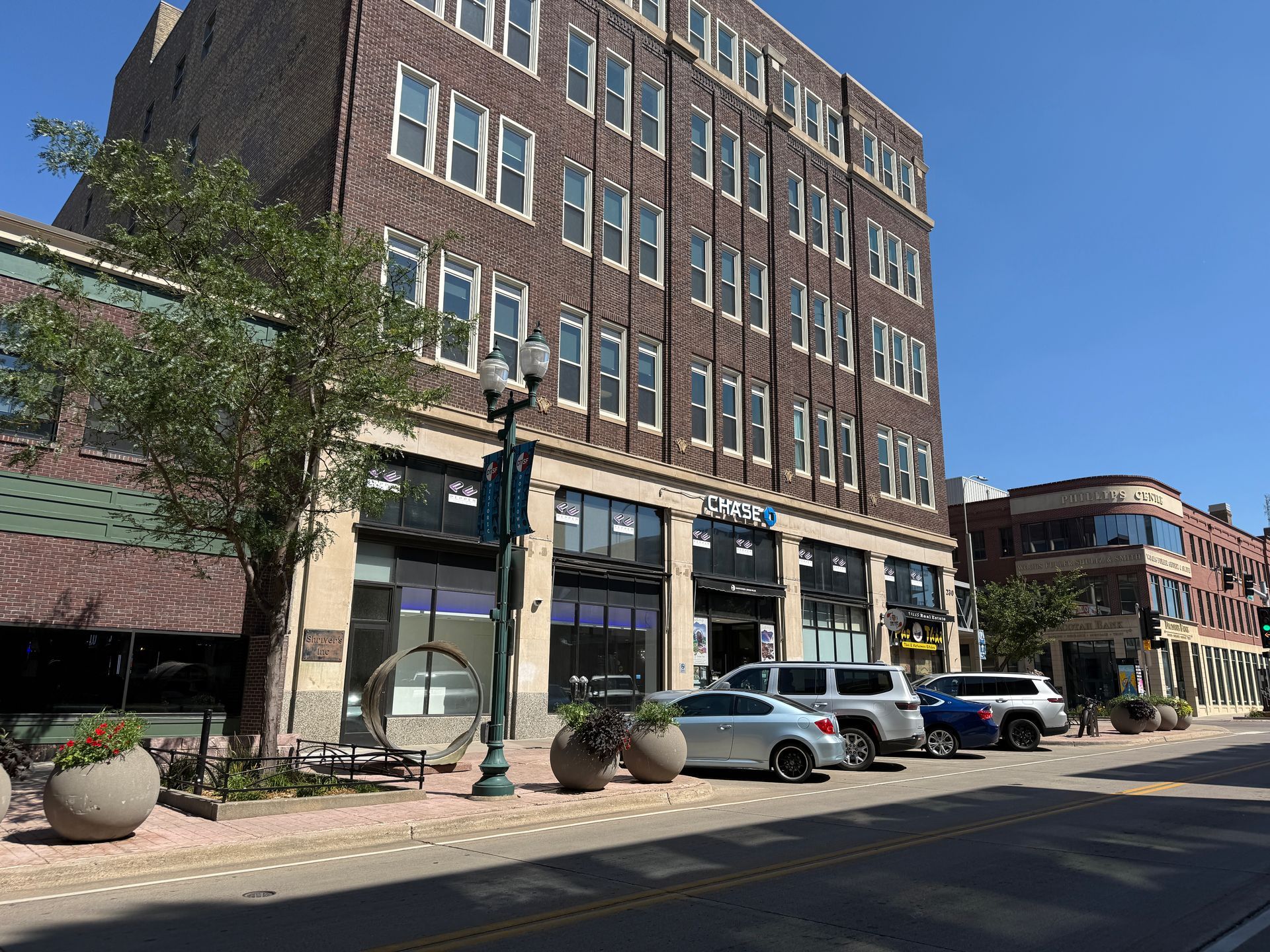 Brick storefronts and parked cars on a sunny downtown street under a clear blue sky