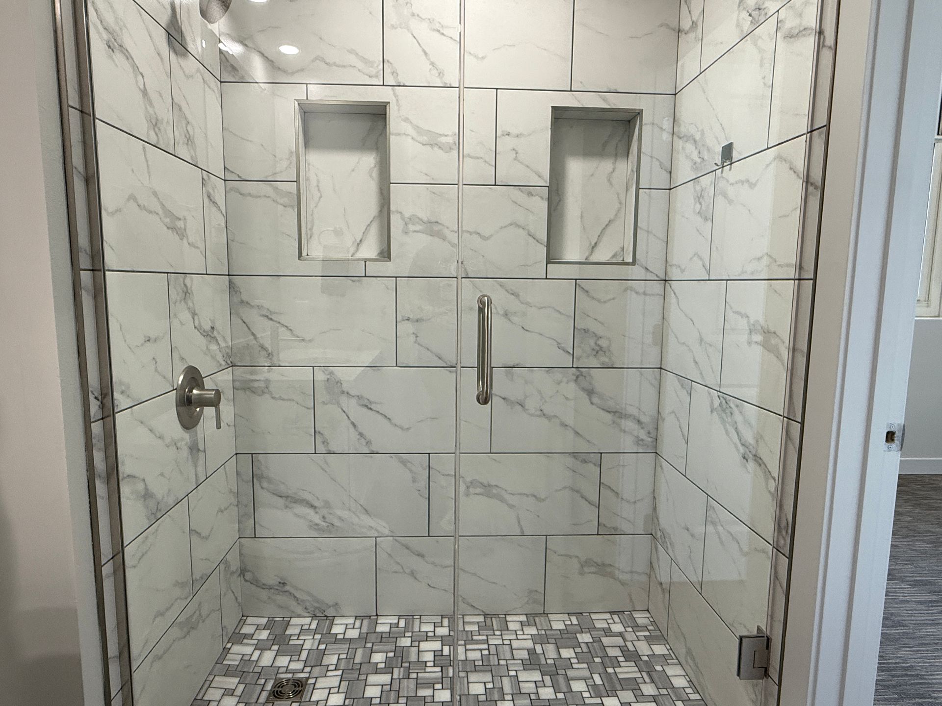 Modern walk-in shower with marble tile walls, niche shelves, and mosaic floor tiles