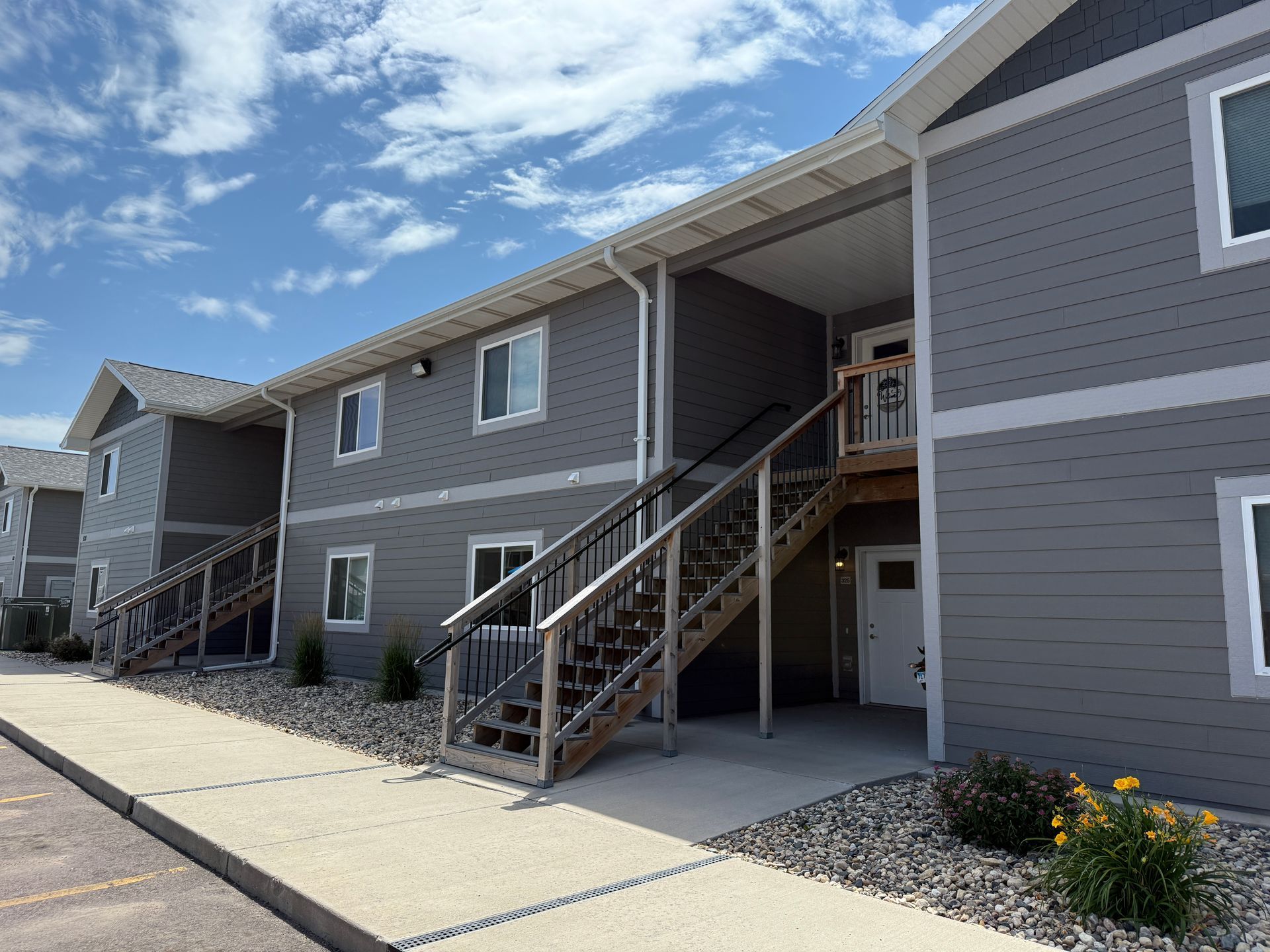 Apartment building exterior with gray siding, exterior staircases, and a blue sky