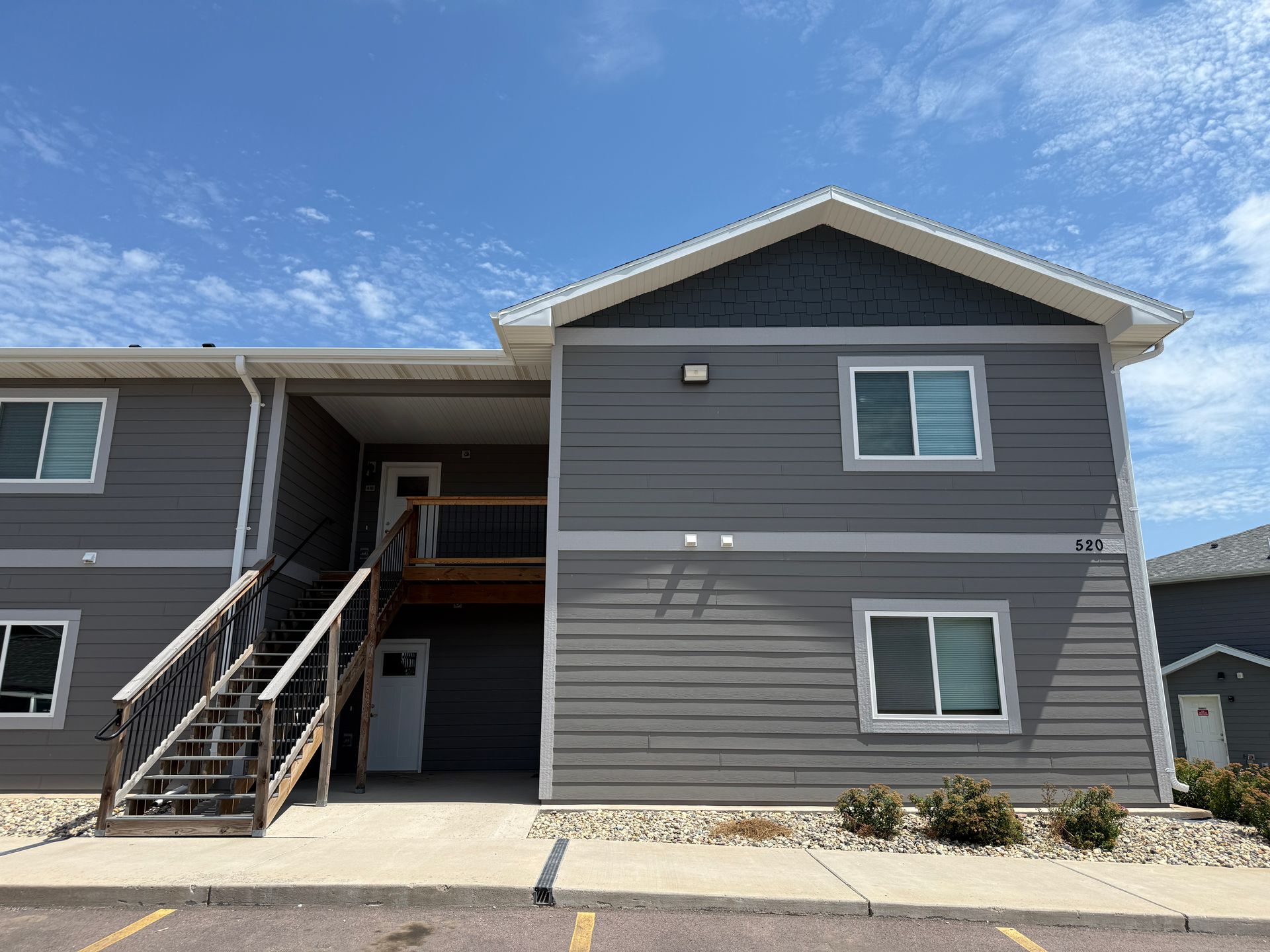 Gray apartment building exterior with stairs, balconies, and blue sky.