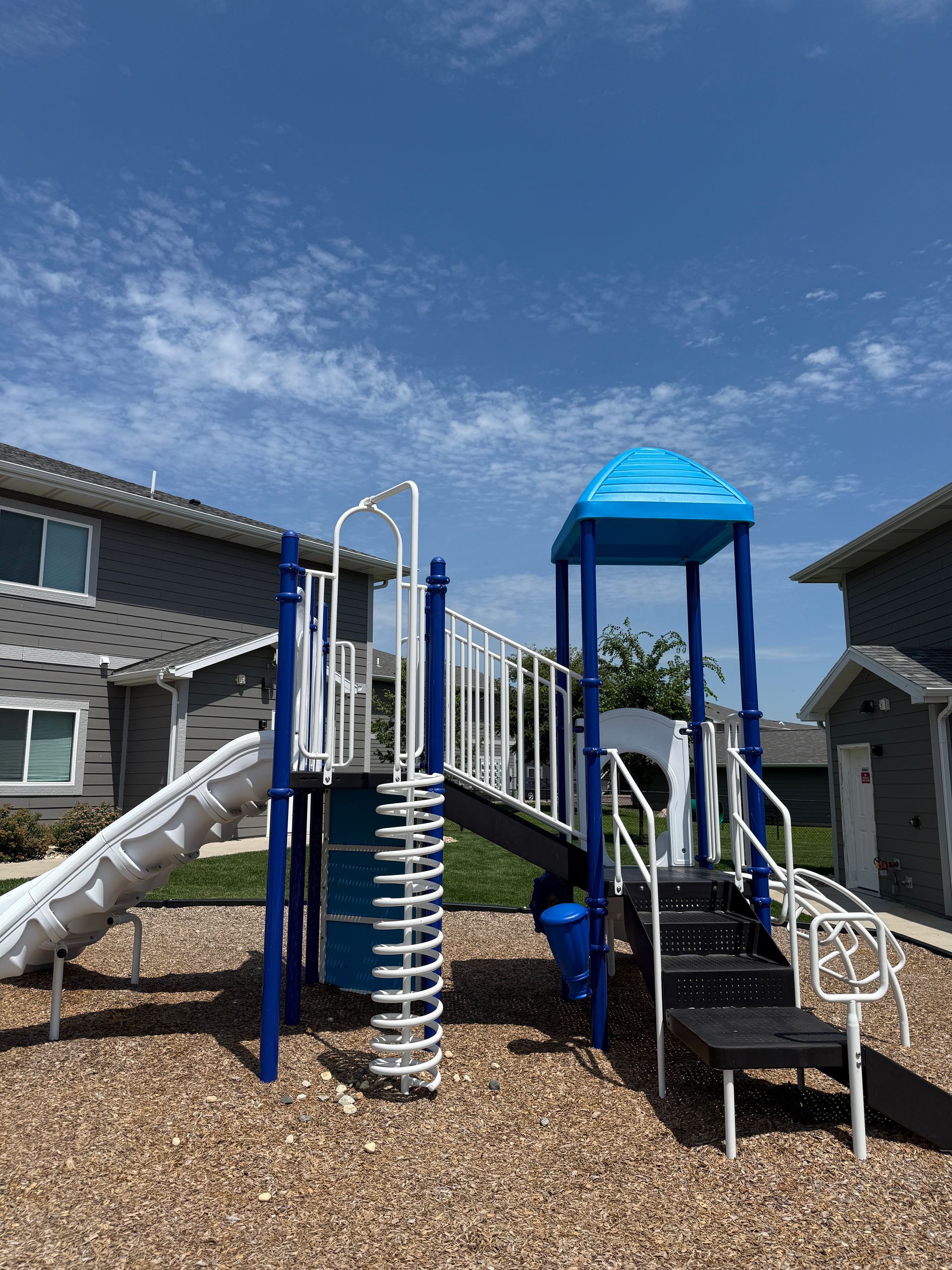 Playground climbing structure with slide, rope bridge, and blue canopy in a residential courtyard