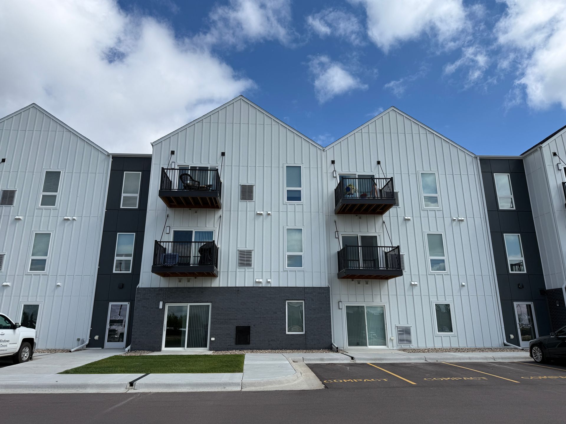 Modern apartment building with balconies, gray siding, and a small parking lot under a cloudy sky