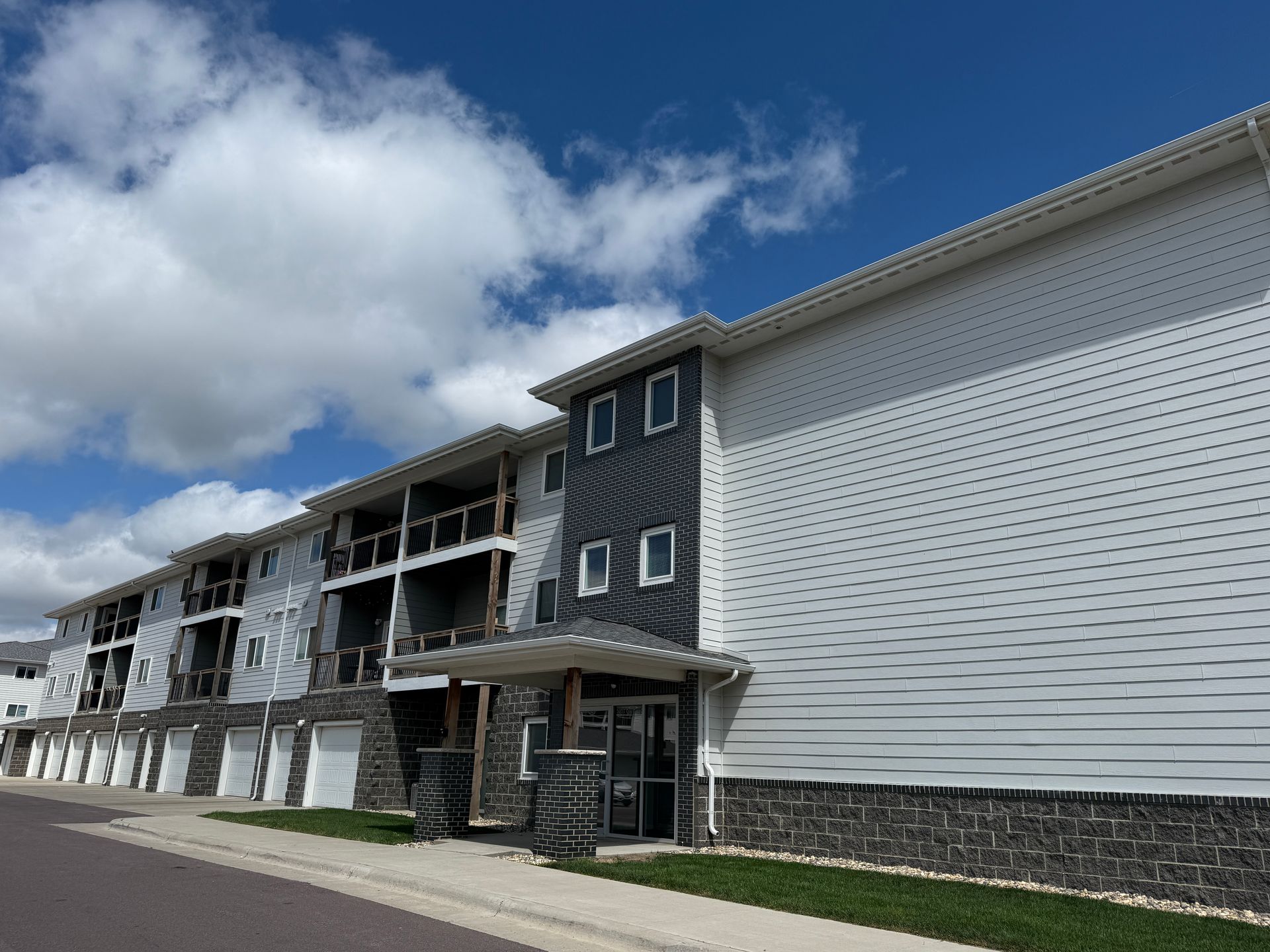 Apartment complex exterior with white siding, dark balconies, and a blue sky with clouds