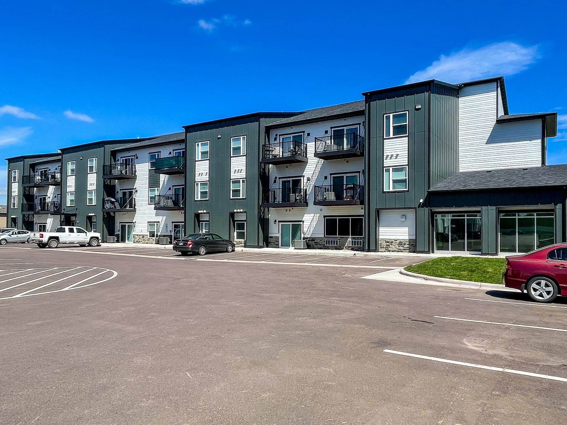 Modern apartment building with balconies and parked cars under a blue sky