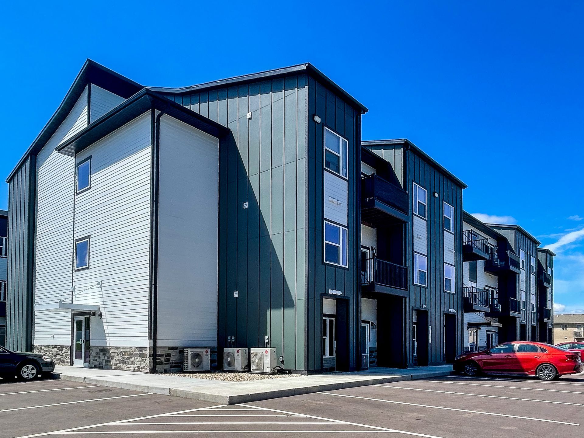 Modern apartment building with dark gray siding and a red car parked outside.