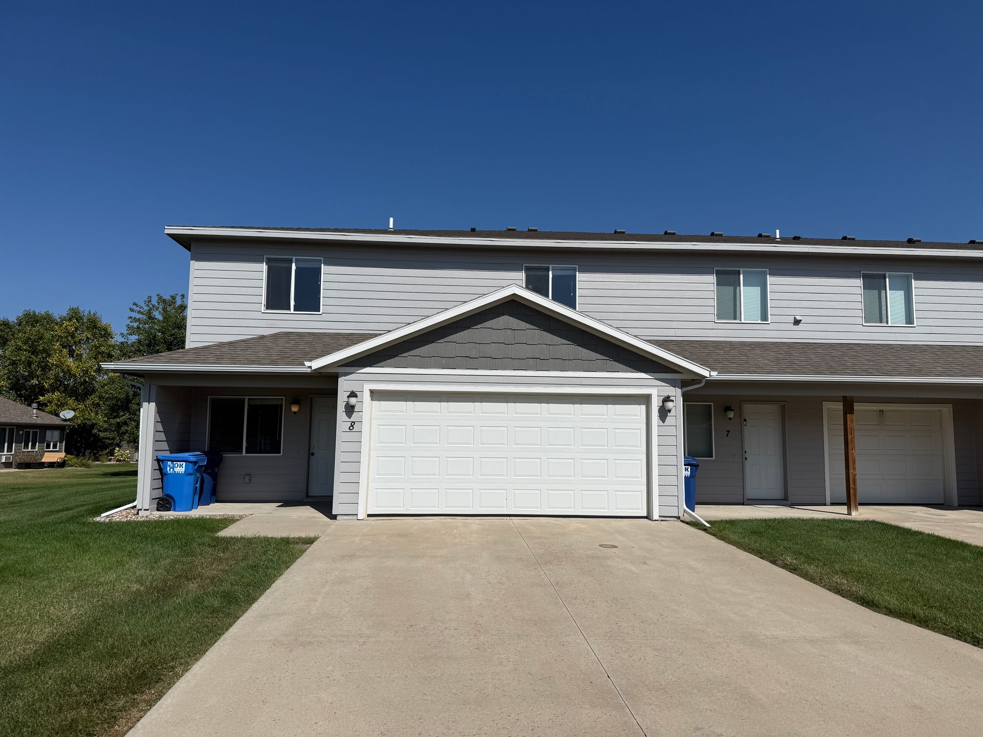 Suburban townhouse with attached garage and driveway under a clear blue sky
