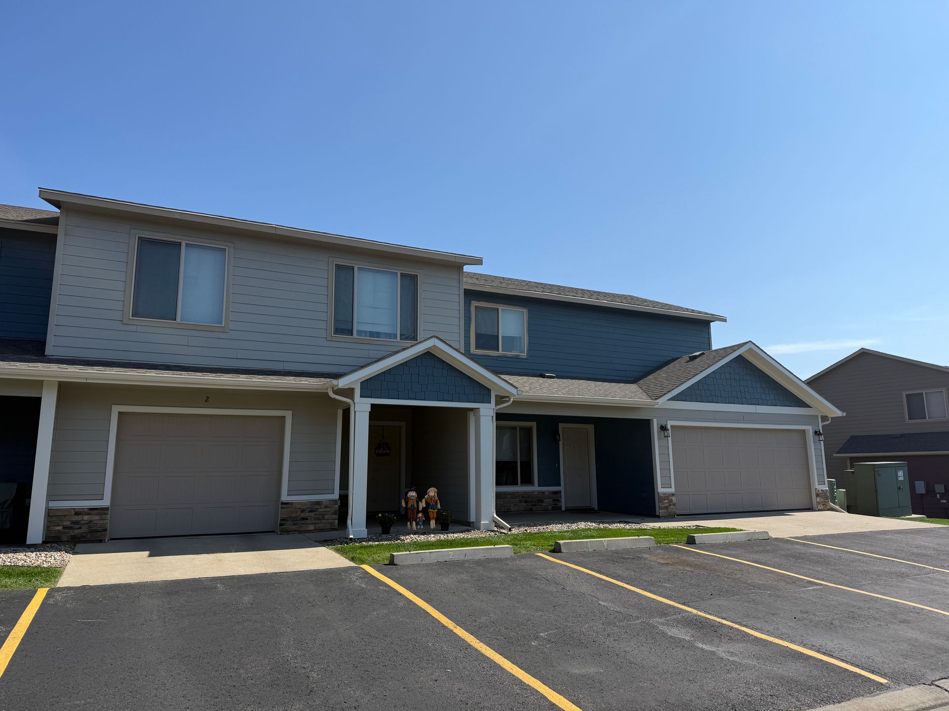 Row of beige townhouses with garages and covered entryways in a sunny parking lot