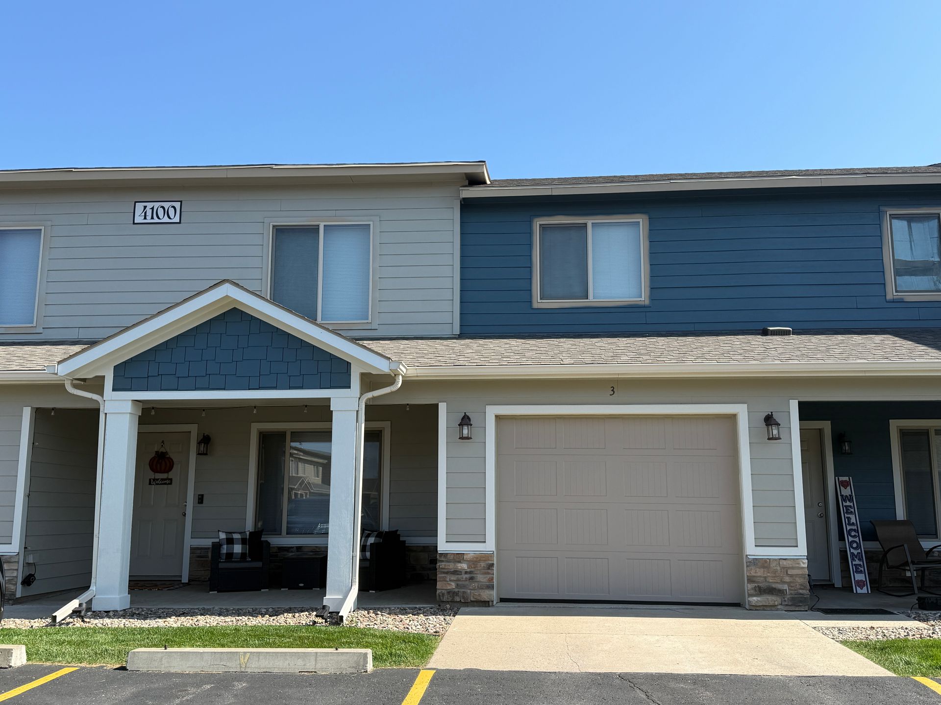 Row of blue townhouses with a white garage, porch, and windows along a grassy front