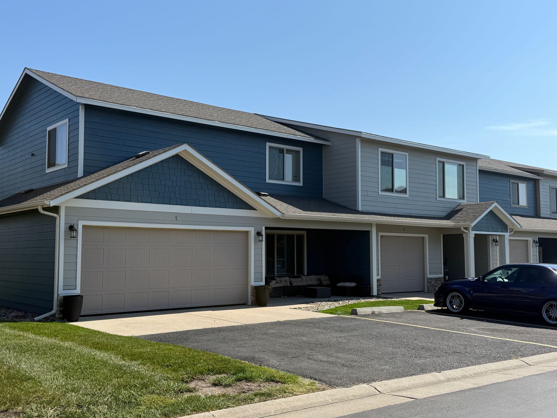 Row of gray townhouses with garages and parked car on a sunny day