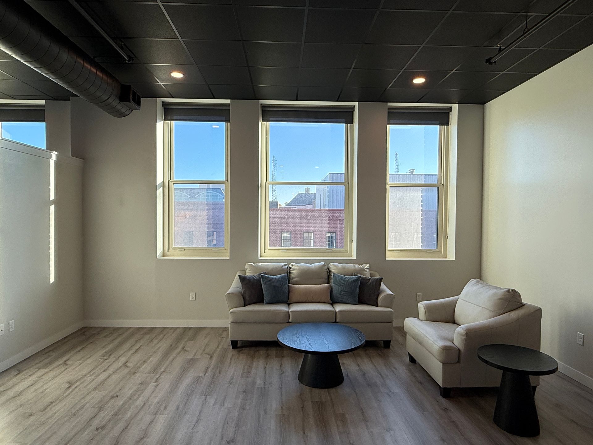 Modern lounge with white armchairs, round tables, and large windows overlooking a city view.