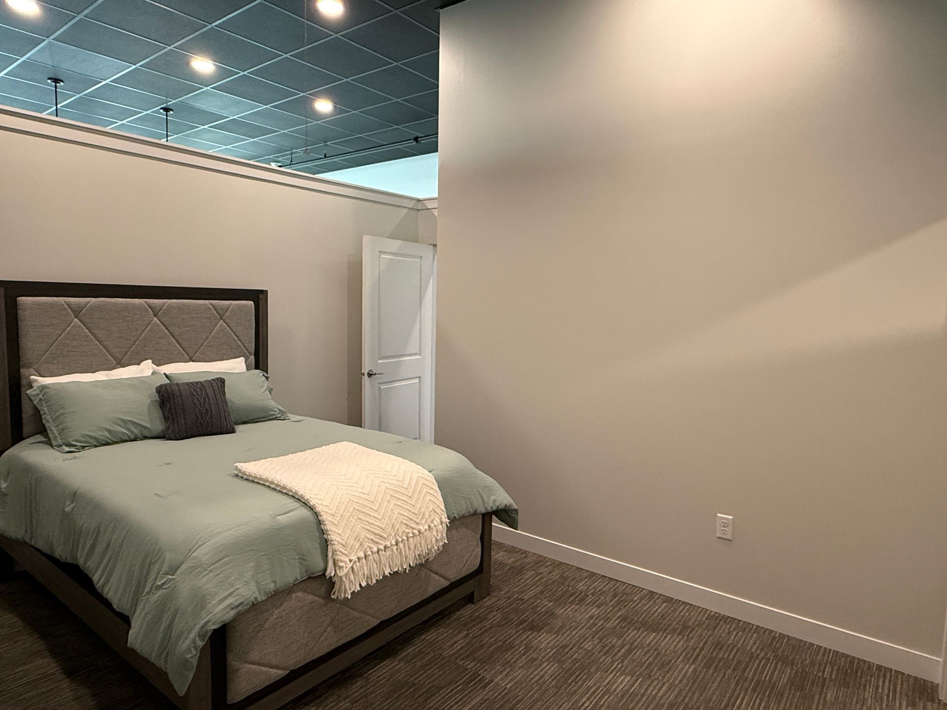 Spare bedroom with a neatly made bed, beige walls, and a blue-tinted ceiling.