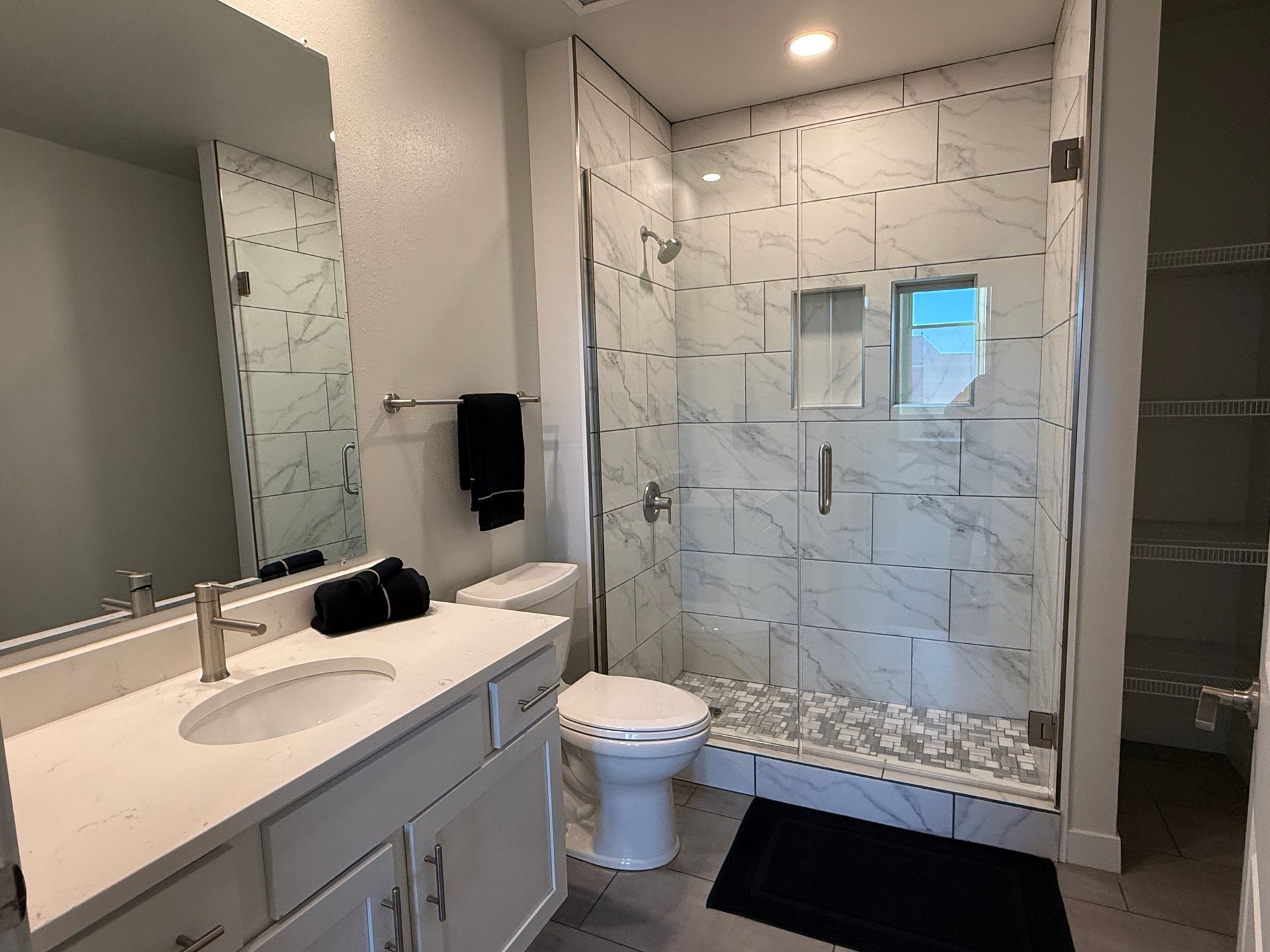 Modern bathroom with double vanity, toilet, and glass walk-in shower with white tile.