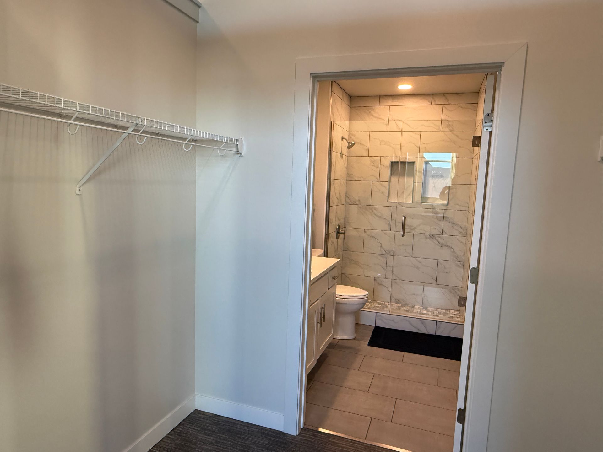 Empty walk-in closet with wire shelving leading to a tiled bathroom with a shower.