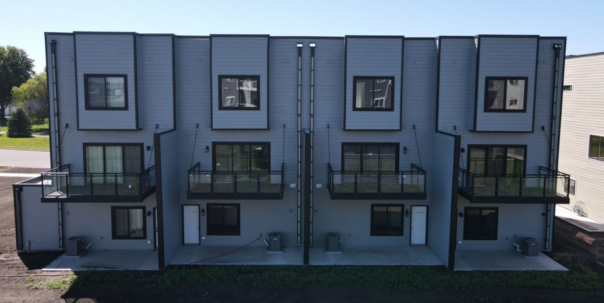 Modern two-story gray apartment building with balconies and black trim in daylight
