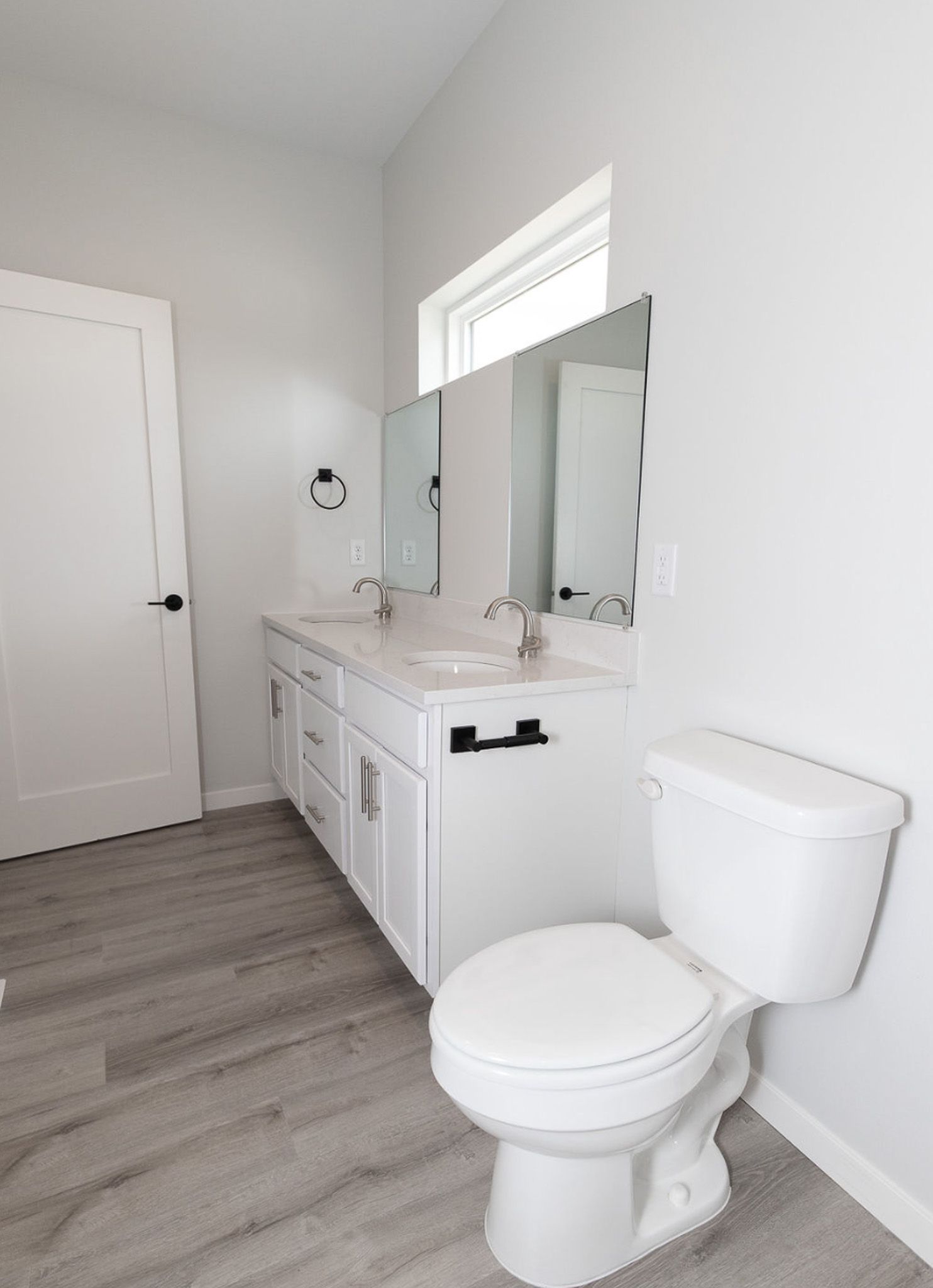 Bright white bathroom with vanity, mirror, toilet, and gray wood-look floor.