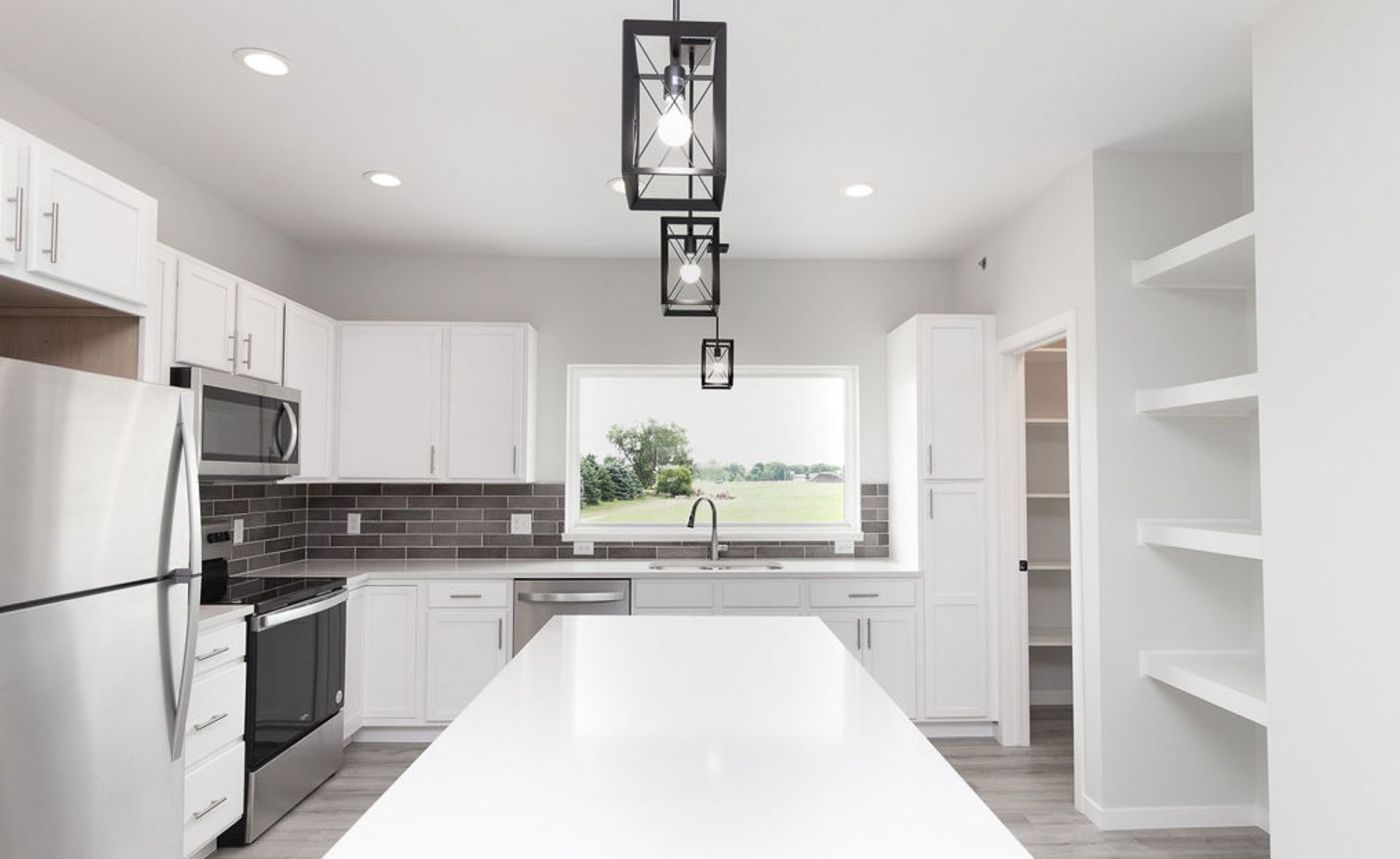 Bright modern white kitchen with island, stainless appliances, dark backsplash, and pendant lights