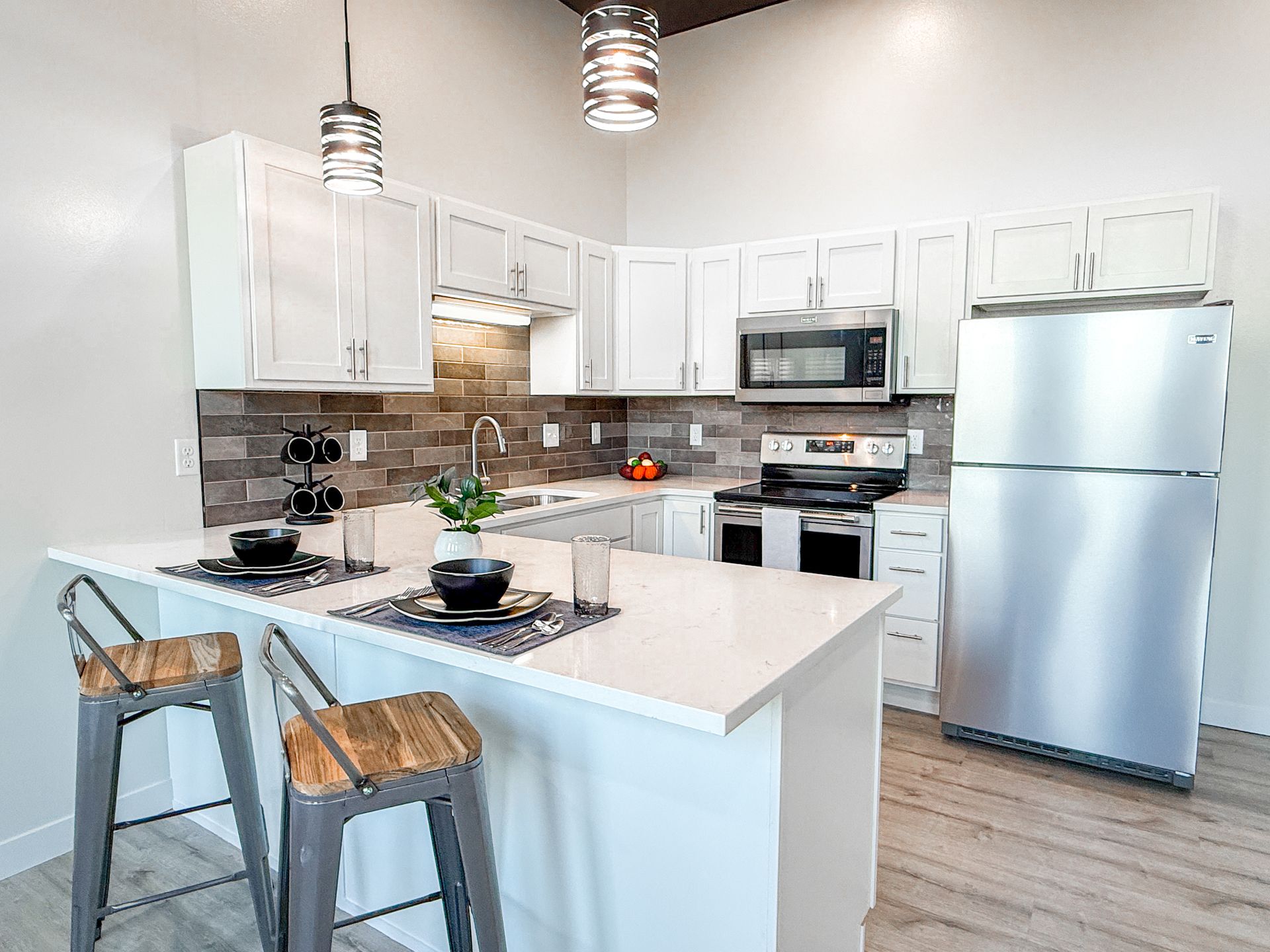 Modern white kitchen with island, stainless appliances, and two wooden bar stools