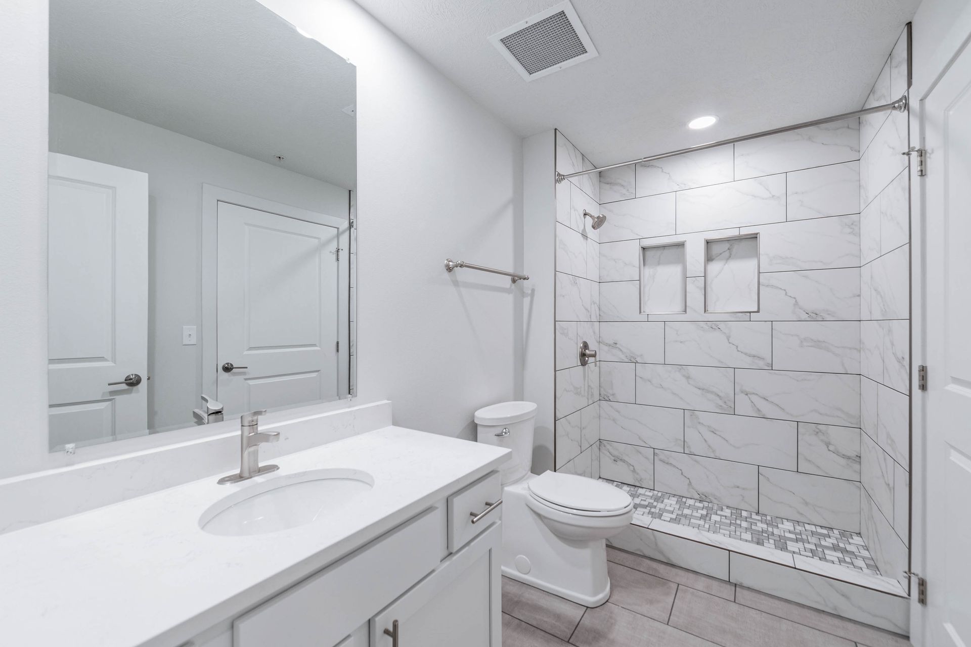 Bright white bathroom with vanity, toilet, and glass shower with marble tile.