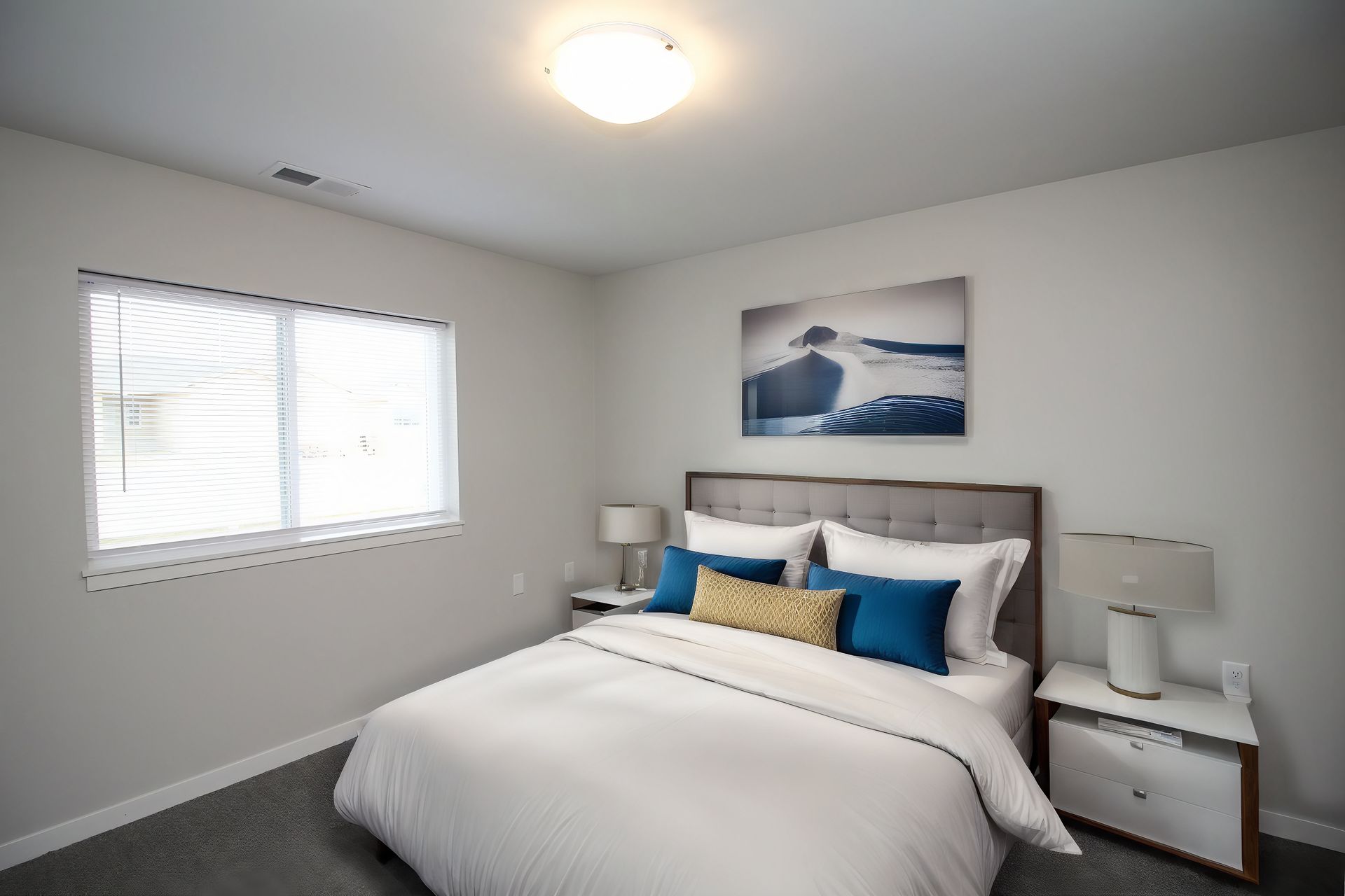 Bright bedroom with a bed, nightstands, lamps, window blinds, and a framed wall print.