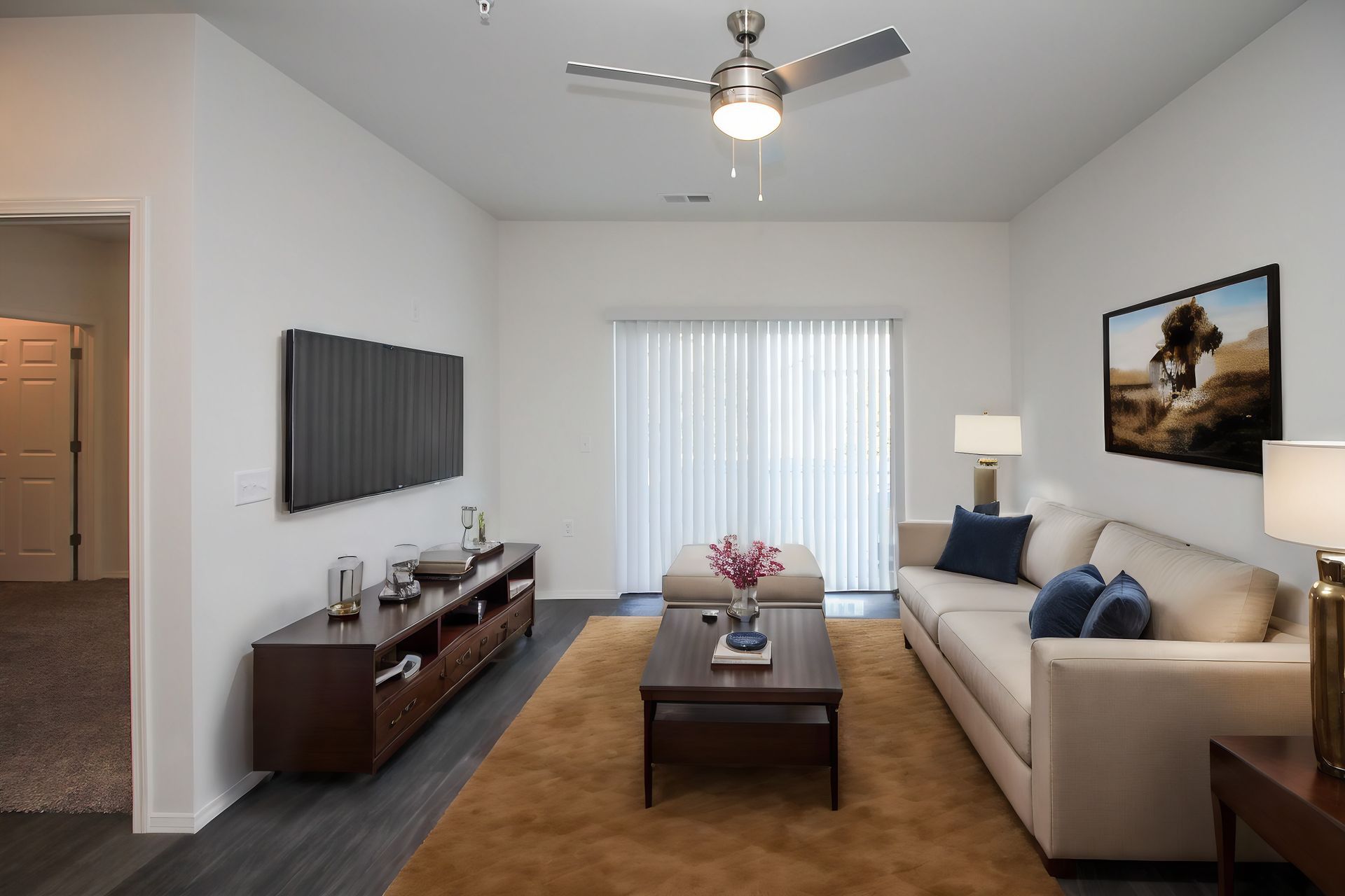 Modern living room with beige sofa, wall-mounted TV, coffee table, and sliding glass door with vertical blinds