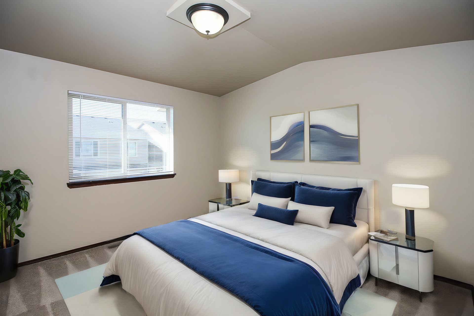 Blue-and-white bedroom with a neatly made bed, two nightstands, lamps, wall art, and a window with blinds