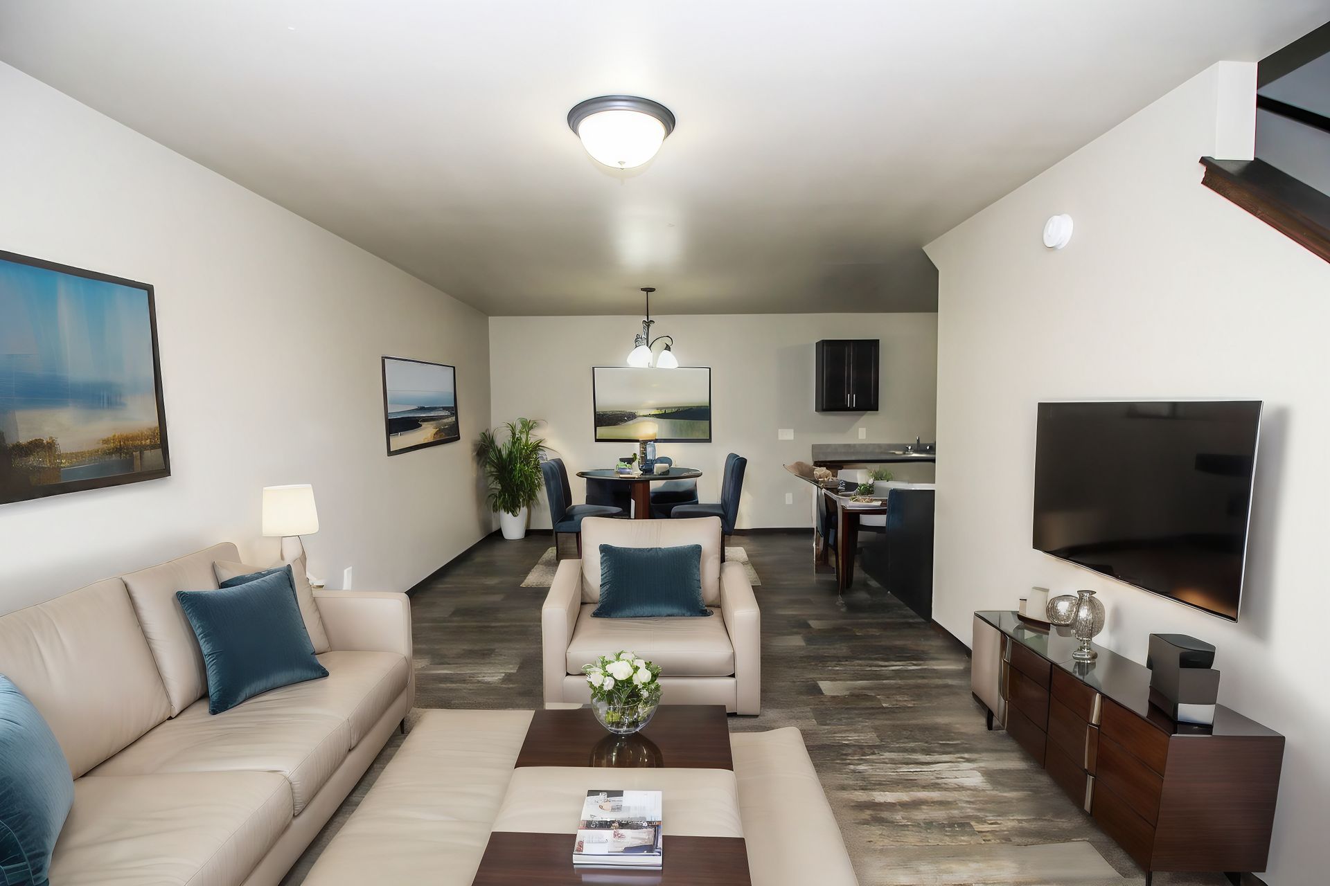 Bright living room with beige sofas, wall-mounted TV, coffee table, and dining area in back