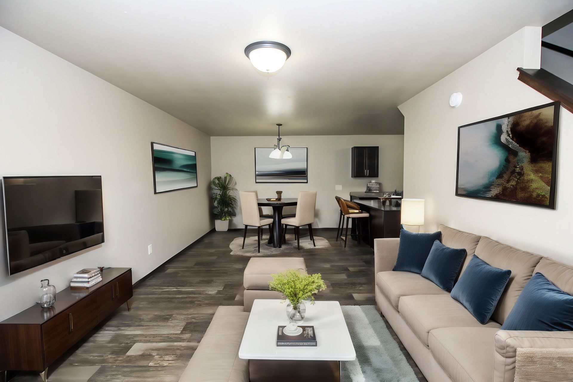 Modern living room with beige sofa, wall-mounted TV, coffee table, and dining area in the background