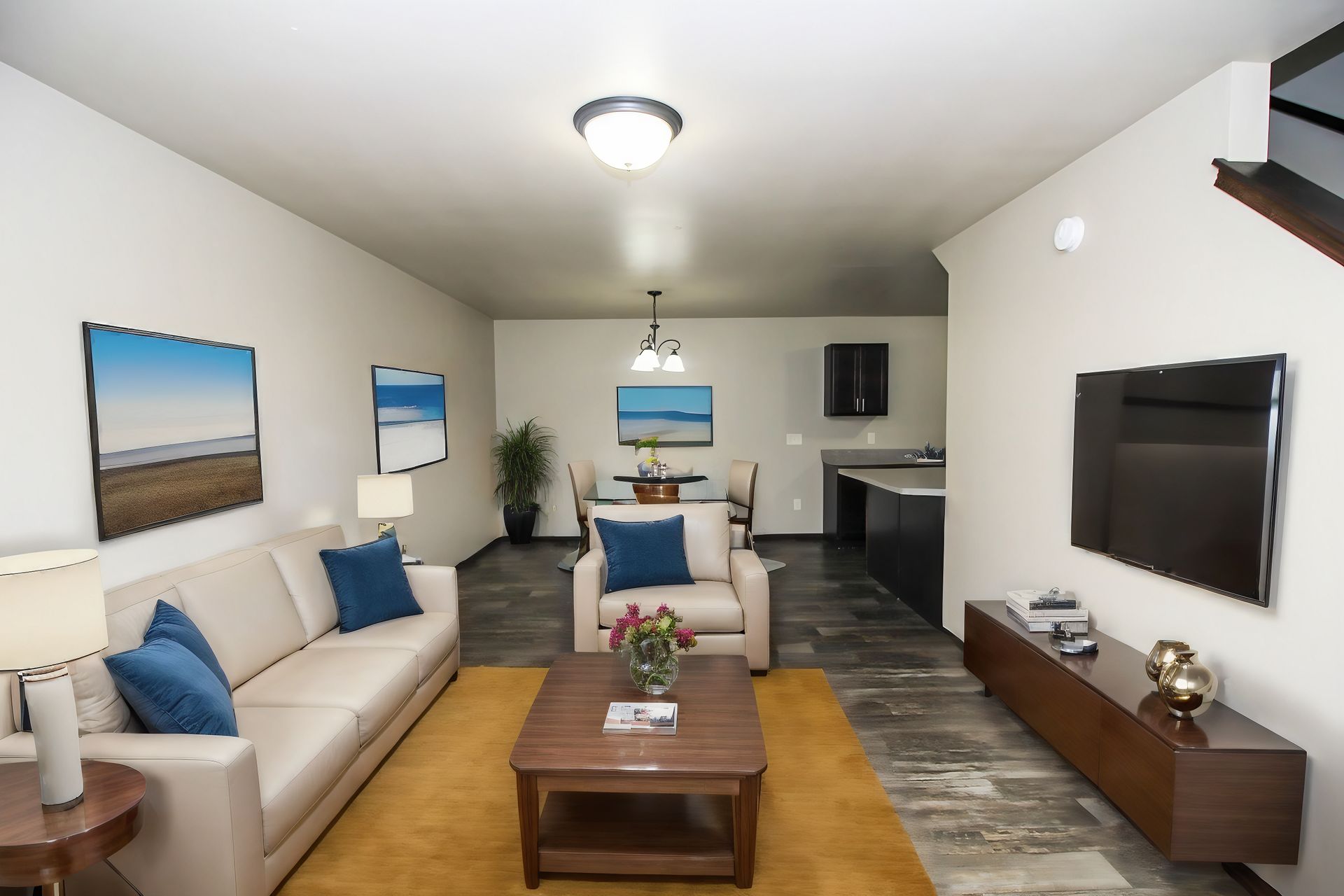 Bright modern living room with beige sofas, blue pillows, wood coffee table, wall art, and a TV.