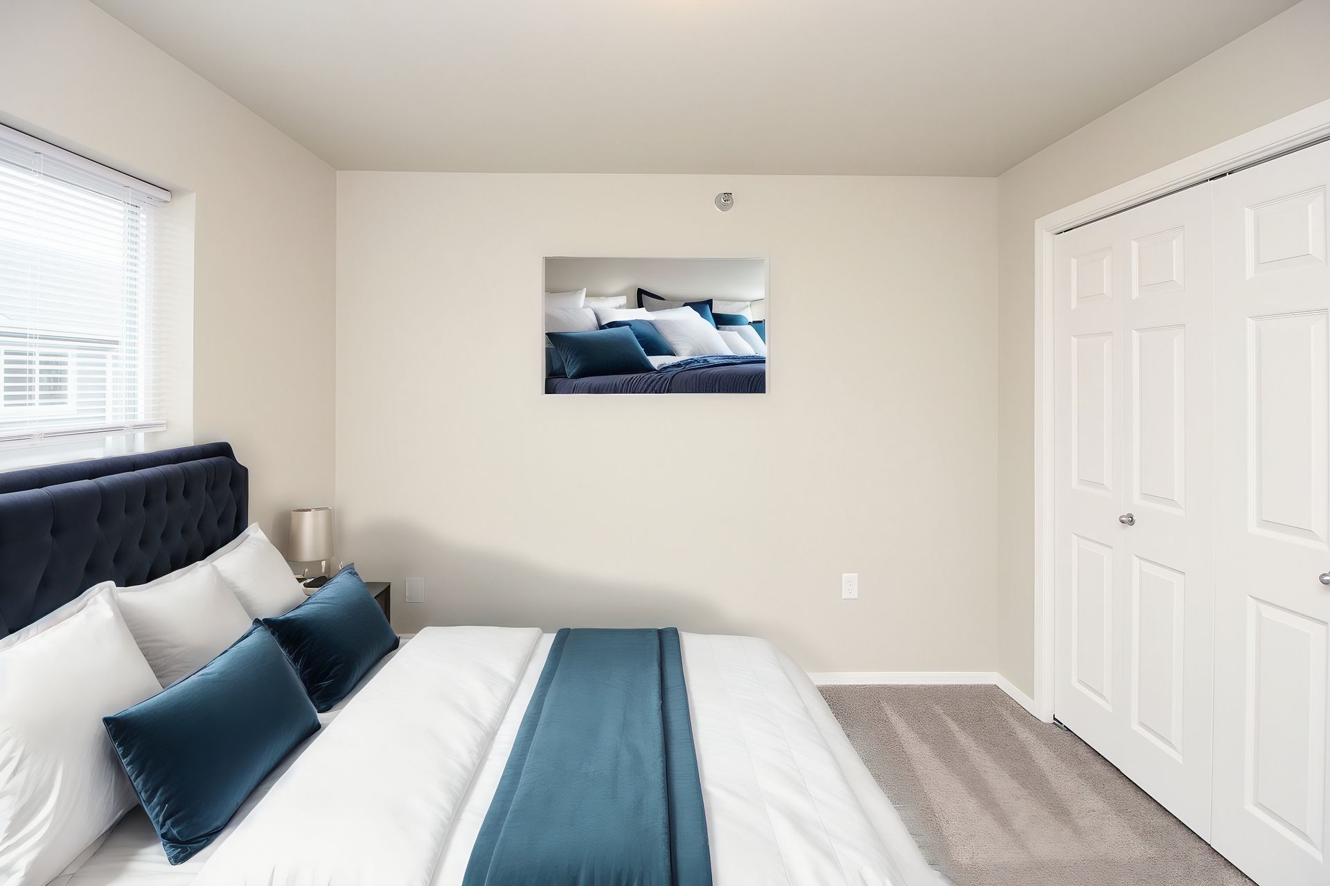 Bright bedroom with navy bed, white walls, closet doors, window, and ocean wall art