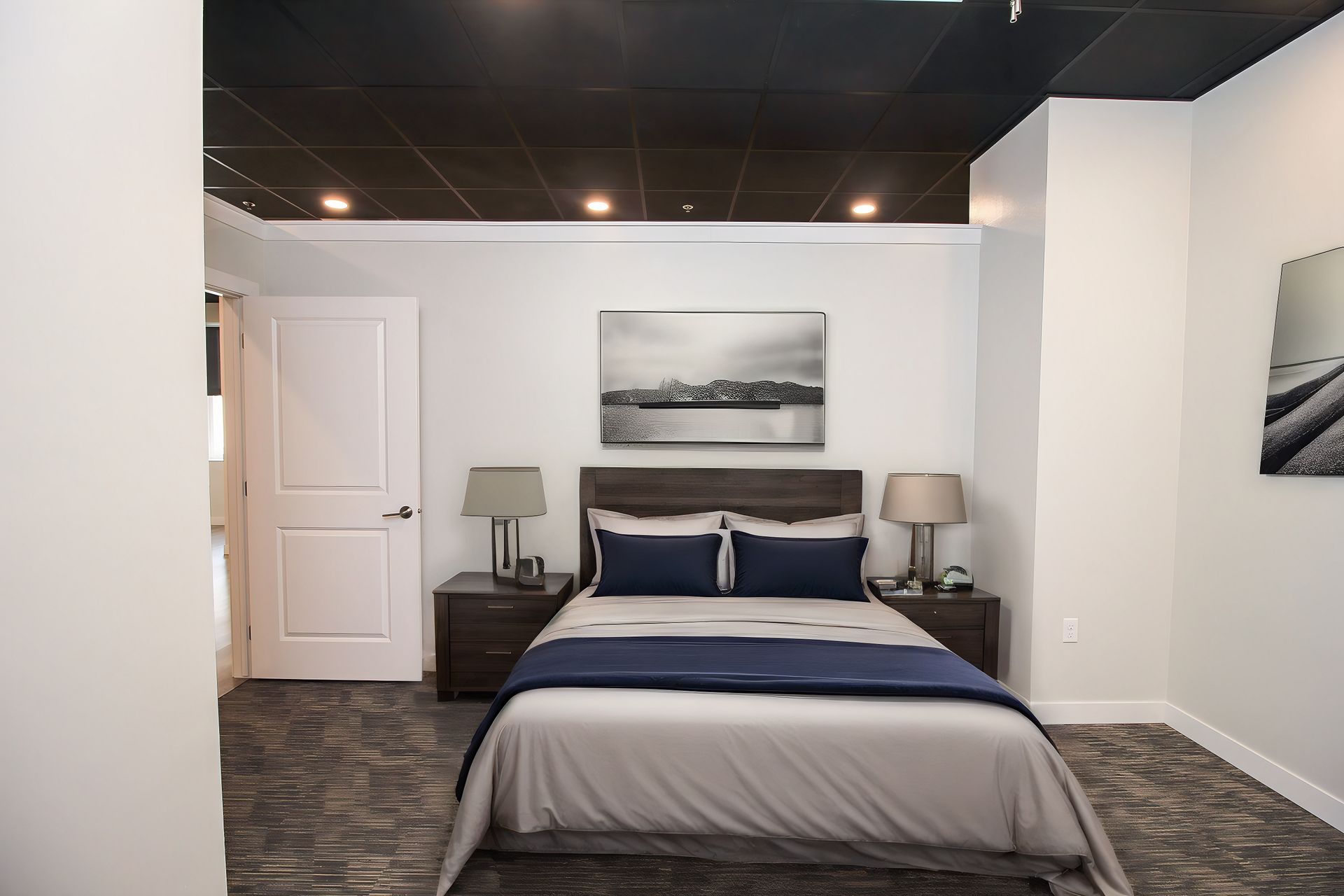 Modern bedroom with a neatly made bed, two nightstands, lamps, and a landscape print above the headboard
