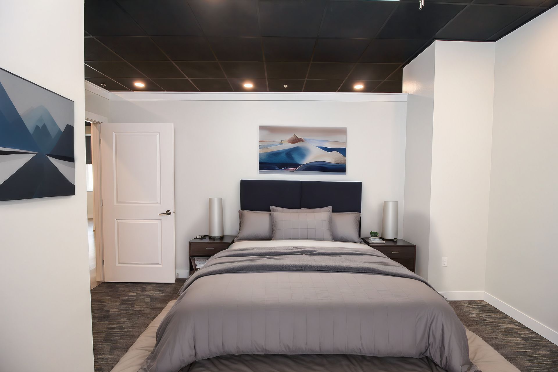 Modern bedroom with a gray bed, wall art, and white walls in a narrow room