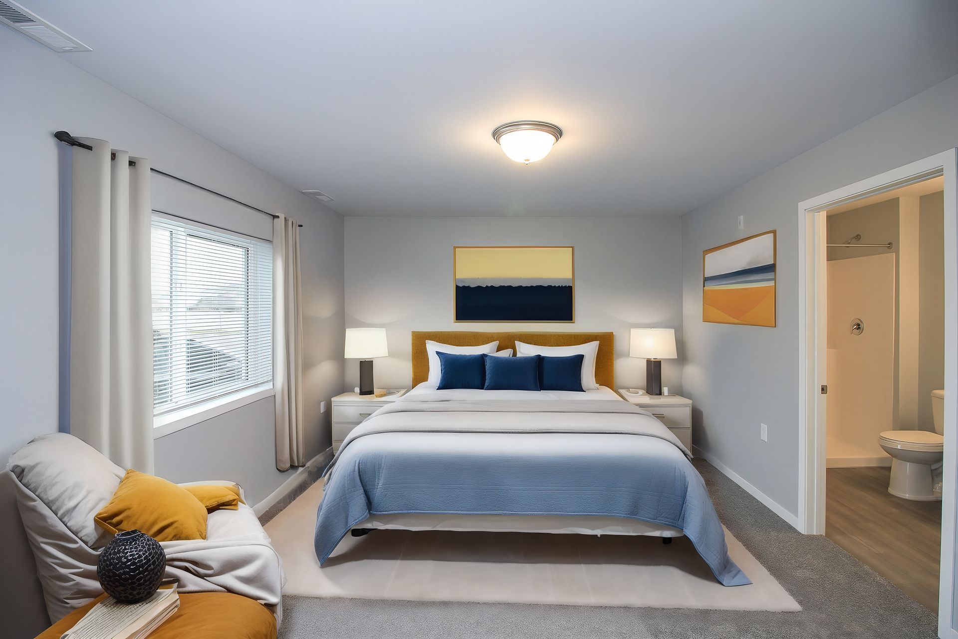 Bright bedroom with a neatly made bed, gray walls, a window seat, and an adjoining bathroom doorway.