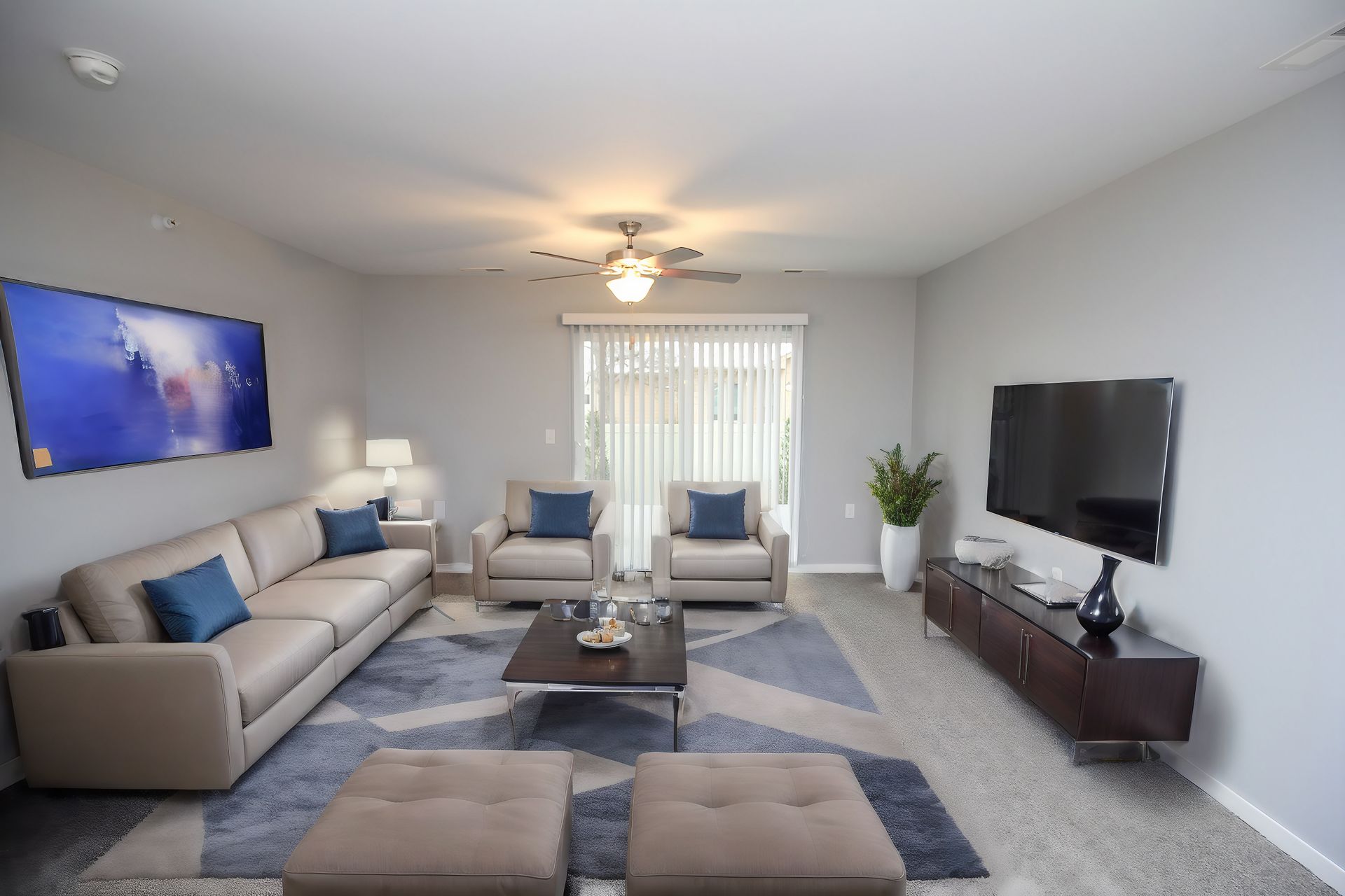 Bright modern living room with gray sofas, blue rug, wall-mounted TV, and large window blinds.