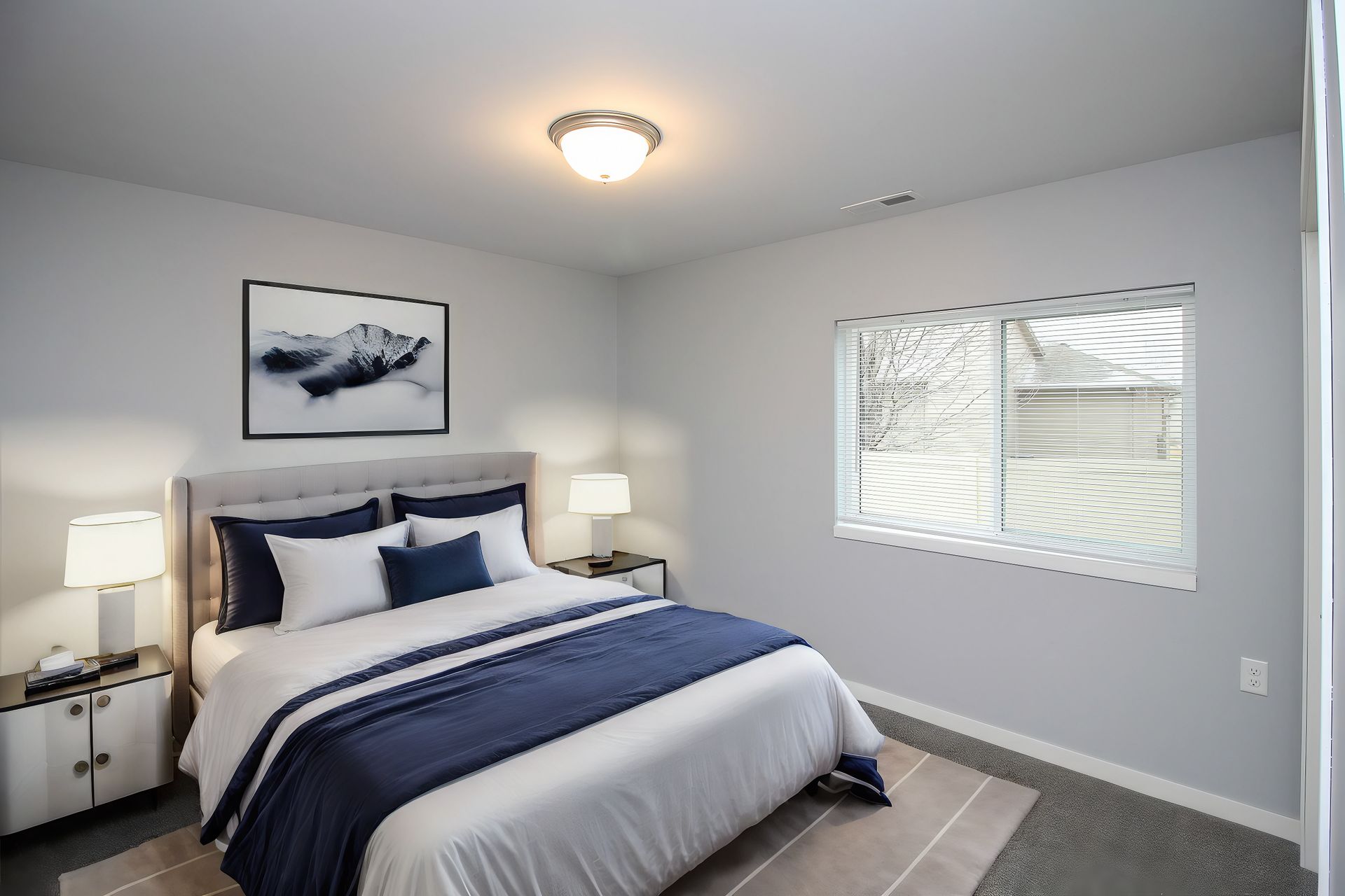 Bright bedroom with a queen bed, navy accents, bedside lamps, and a window with blinds