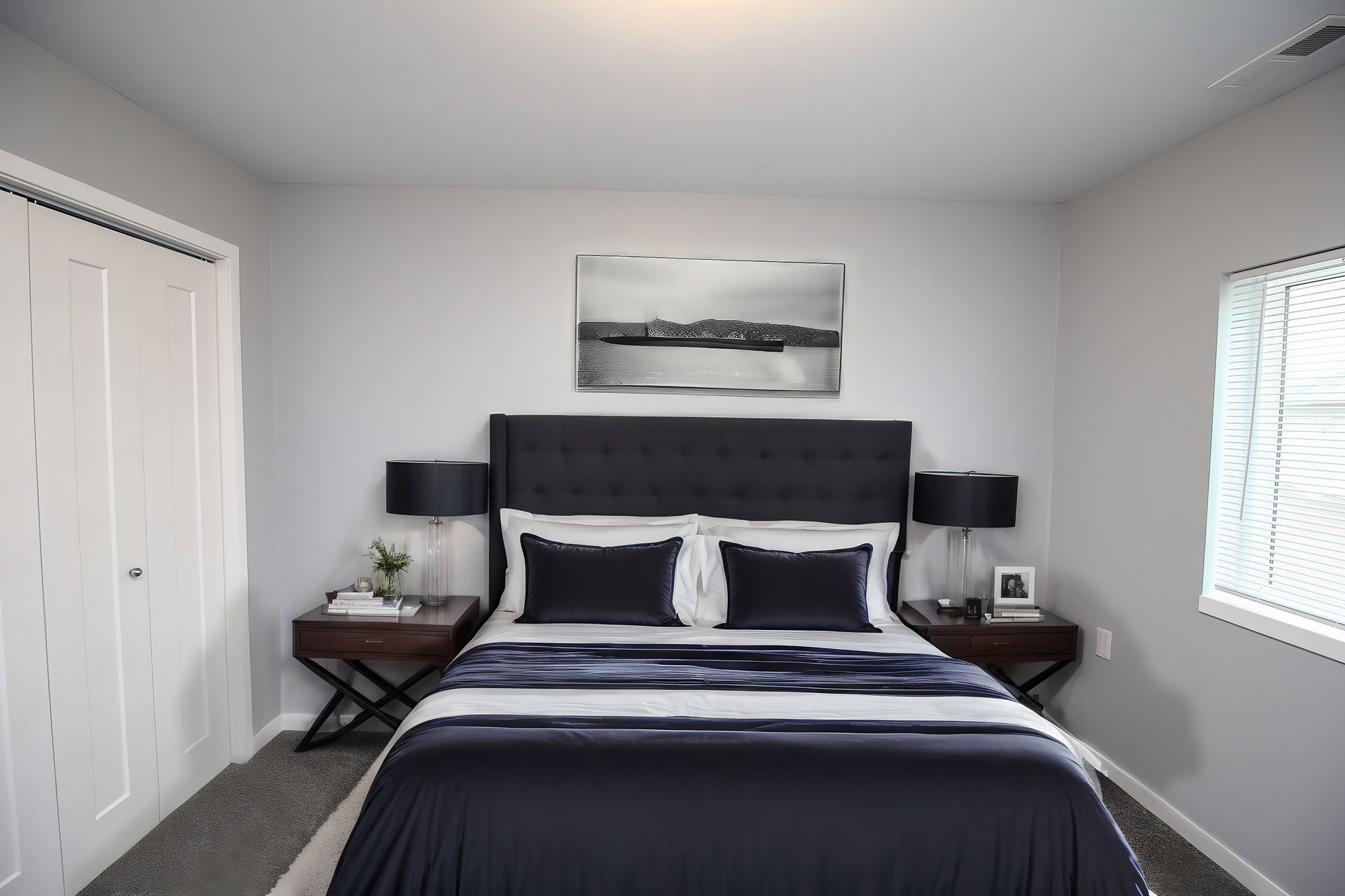Bright bedroom with a neatly made dark bed, bedside tables, wall art, and white closet doors and blinds.
