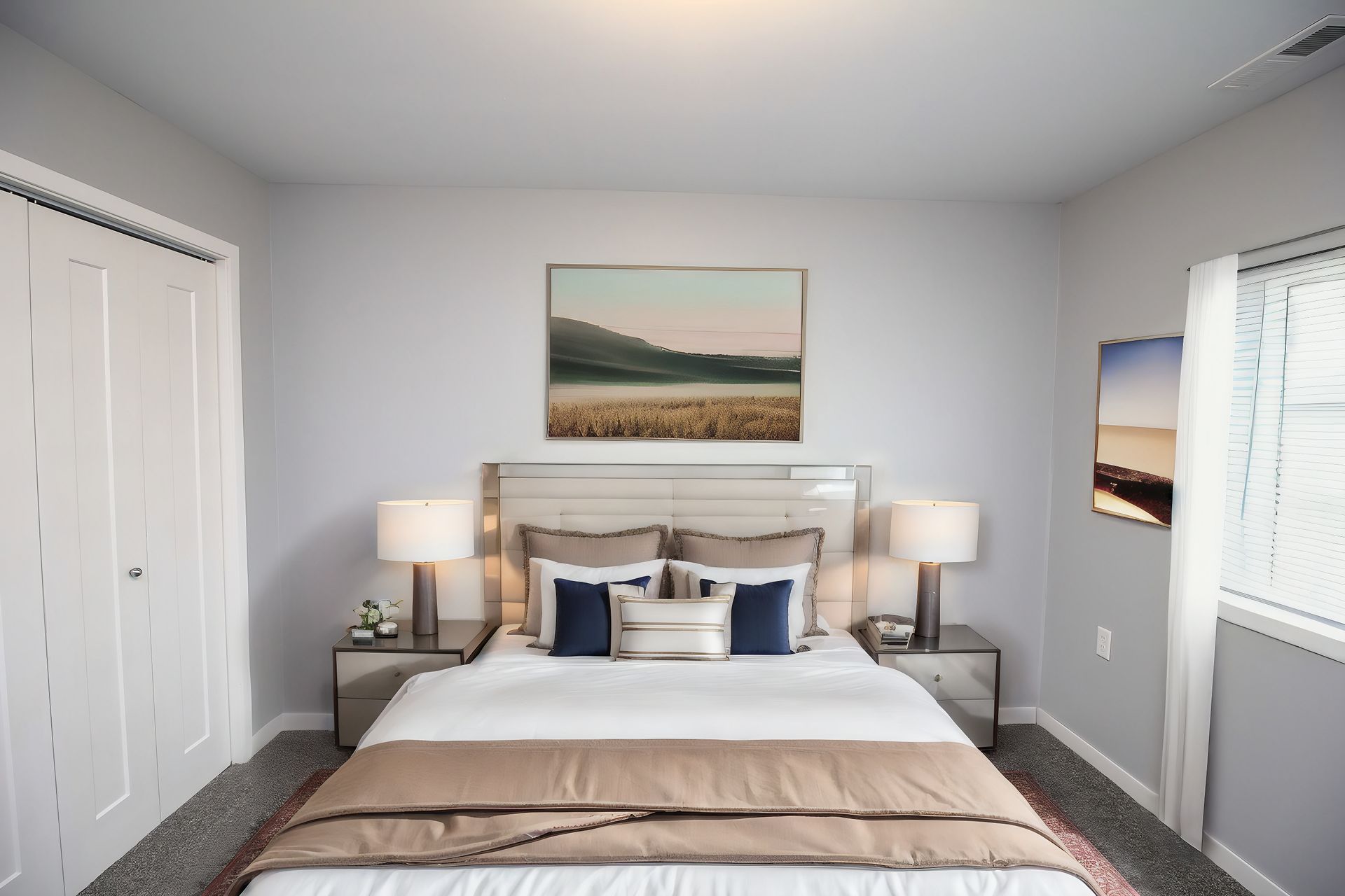 Bright bedroom with a white bed, bedside lamps, closet doors, and landscape artwork above the headboard.