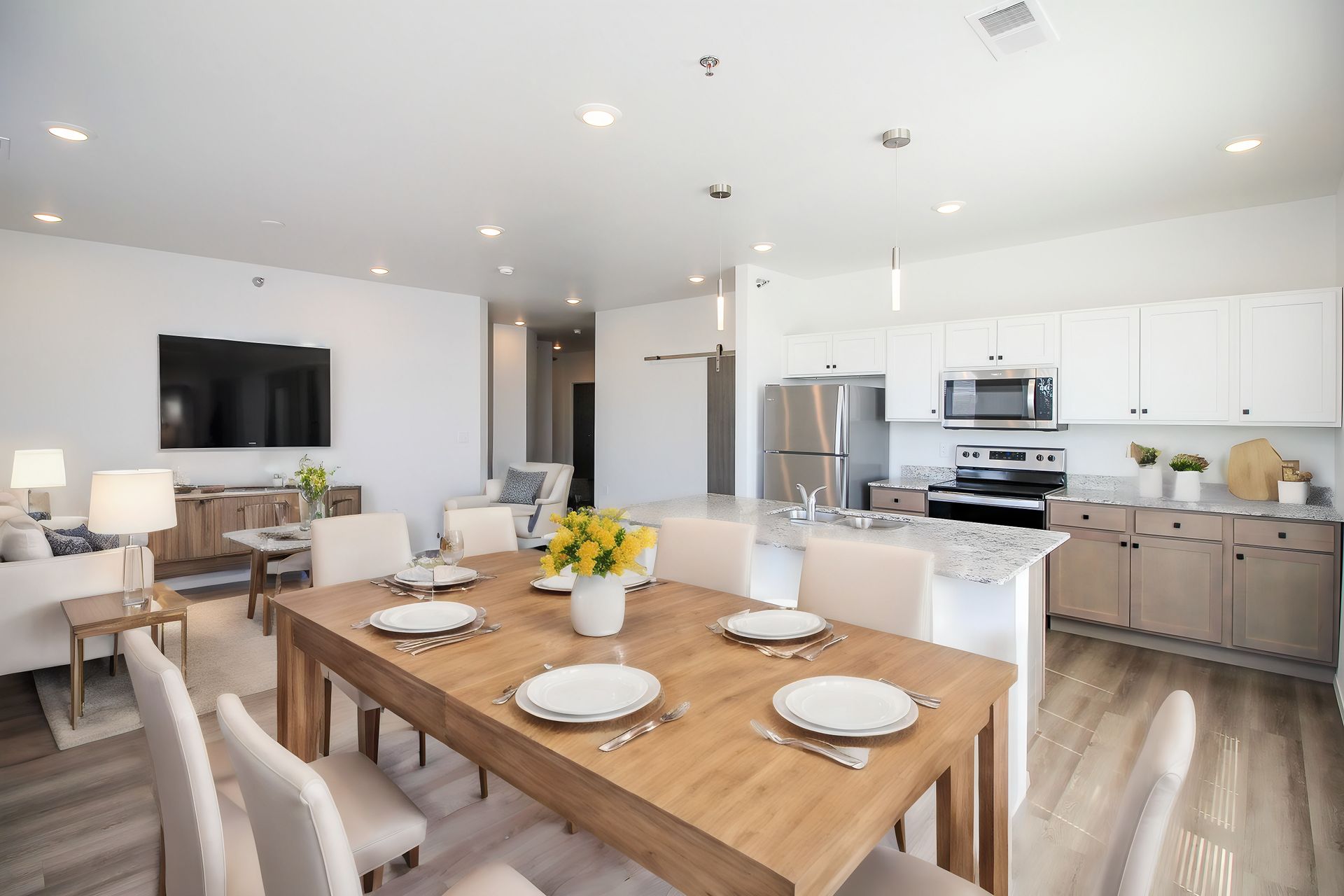 Bright open-plan kitchen and living room with white cabinets, island stools, blue chairs, and a round table