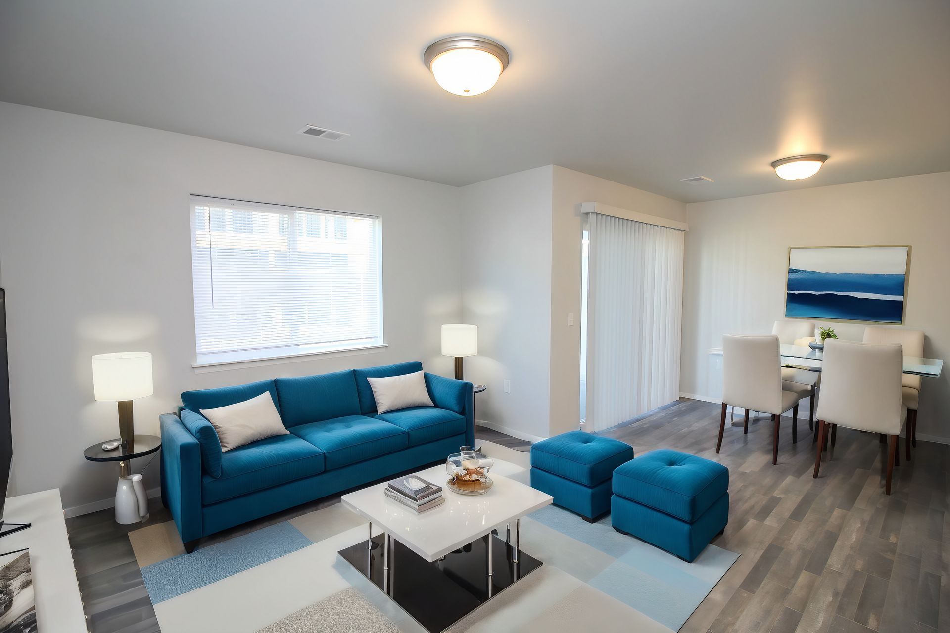 Bright living room with blue sofa, ottomans, coffee table, and dining area by the window.