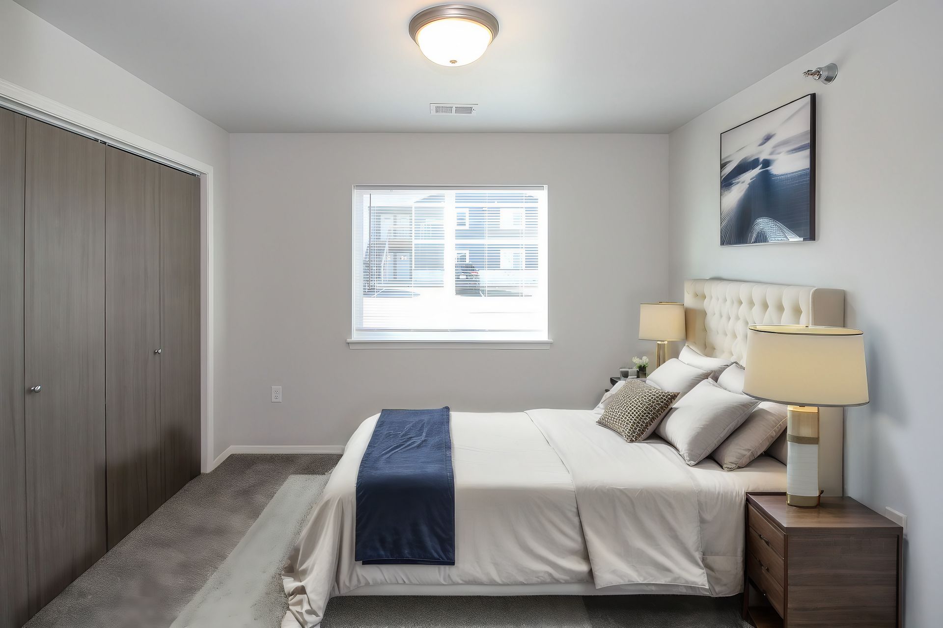 Bright bedroom with a neatly made bed, bedside lamps, window, and closet.