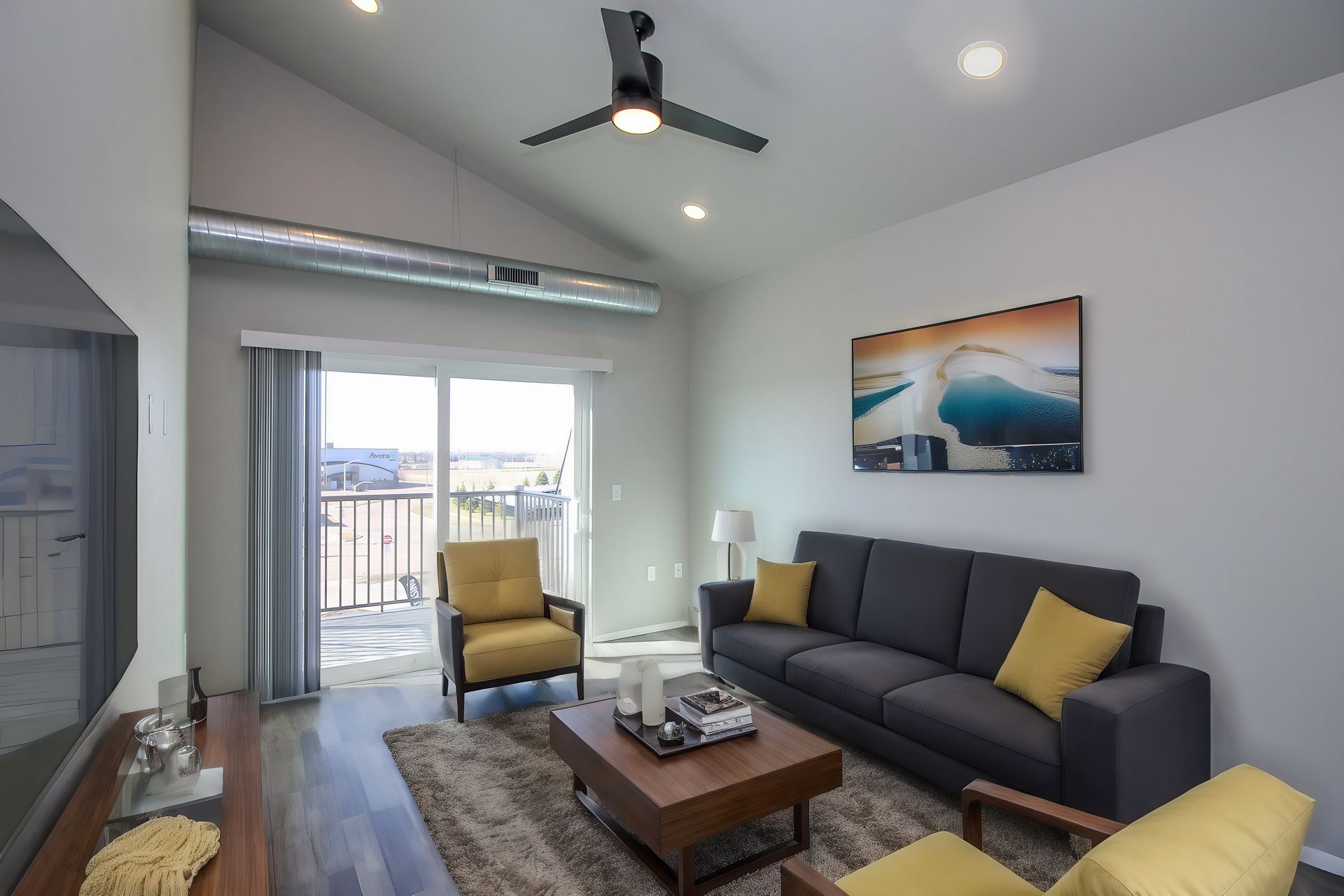 Modern living room with gray sofa, yellow chairs, coffee table, and sliding glass doors to a balcony