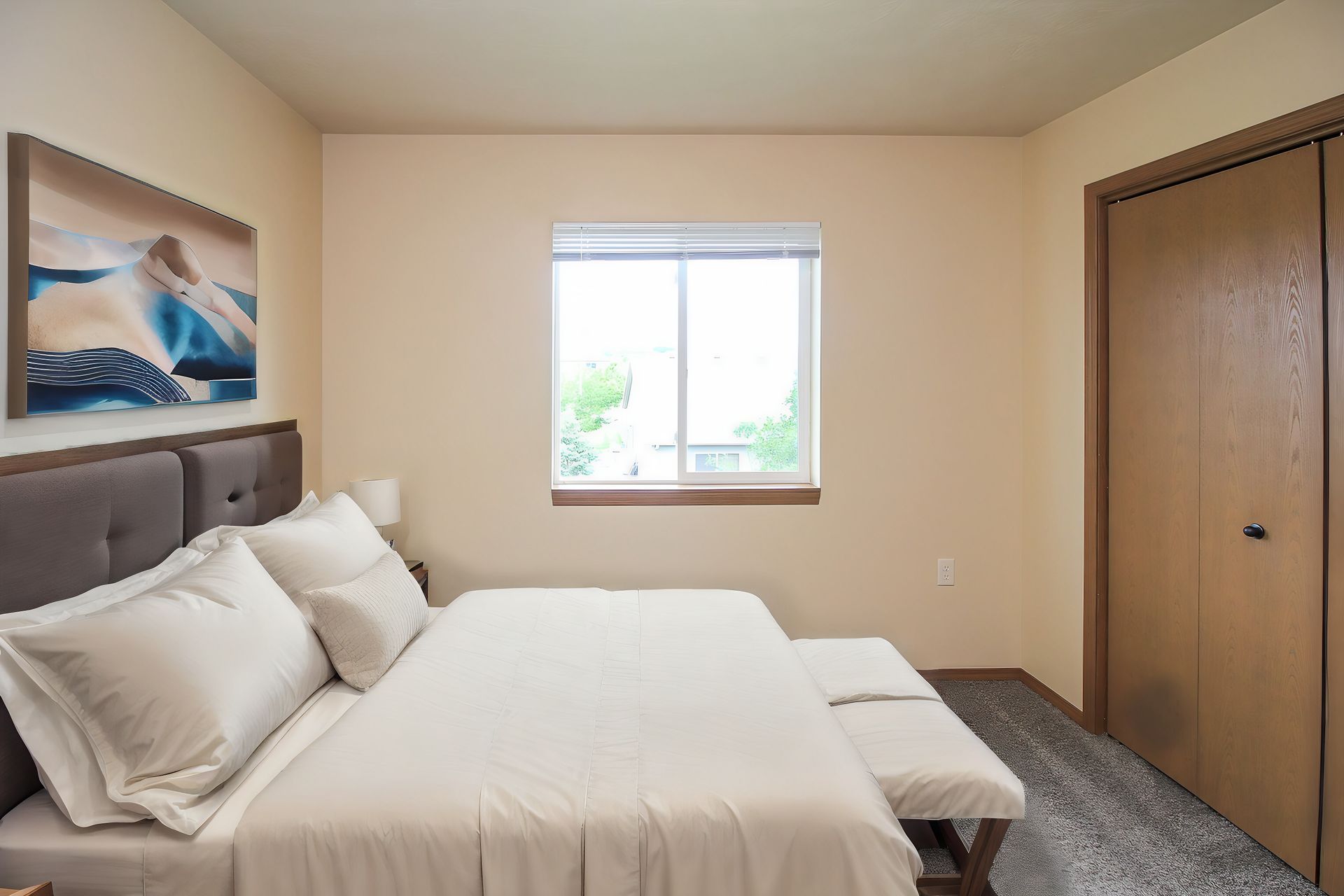 Neatly made bedroom with a bed, window, dresser, and closet in soft neutral tones.